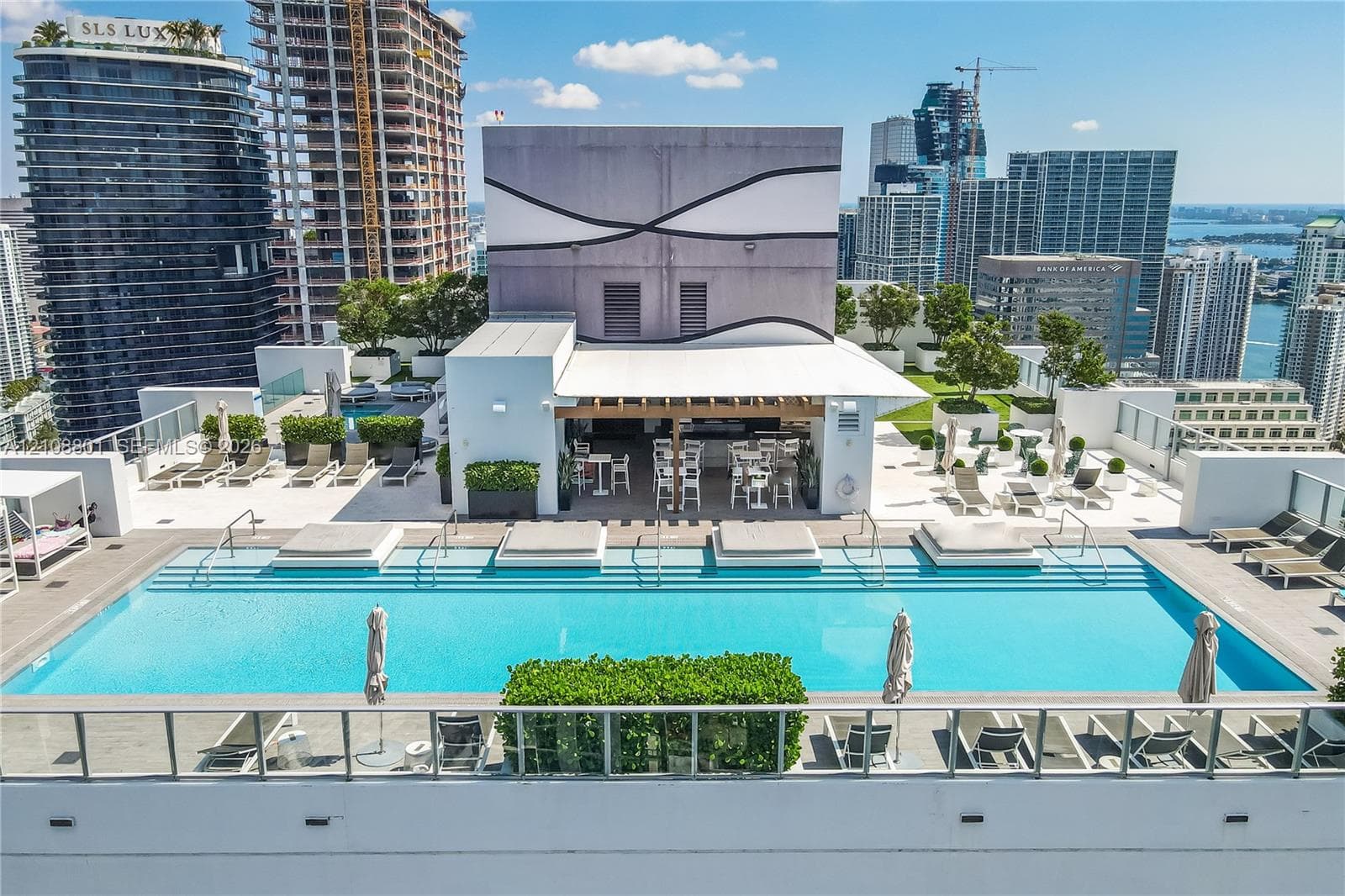 Rooftop swimming pool with integrated sun shelf and glass panel railing, featuring a covered outdoor kitchen, stone-tile decking, and manicured terrace landscaping