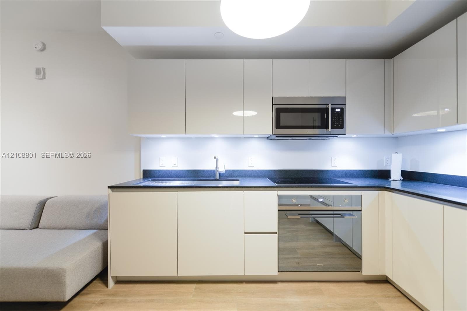 Kitchen featuring high-gloss cabinetry, dark countertops, integrated stainless steel oven, built-in microwave, and wood-finish flooring