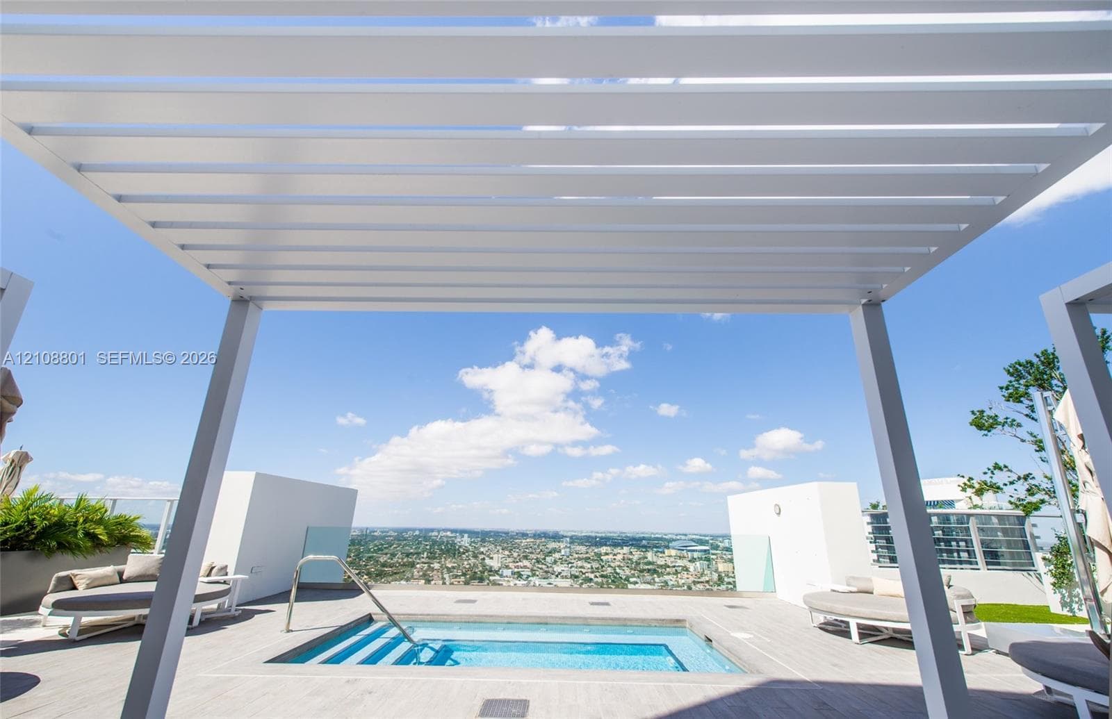 Rooftop terrace featuring a built-in plunge pool, louvered pergola, glass railings, and expansive urban scenery