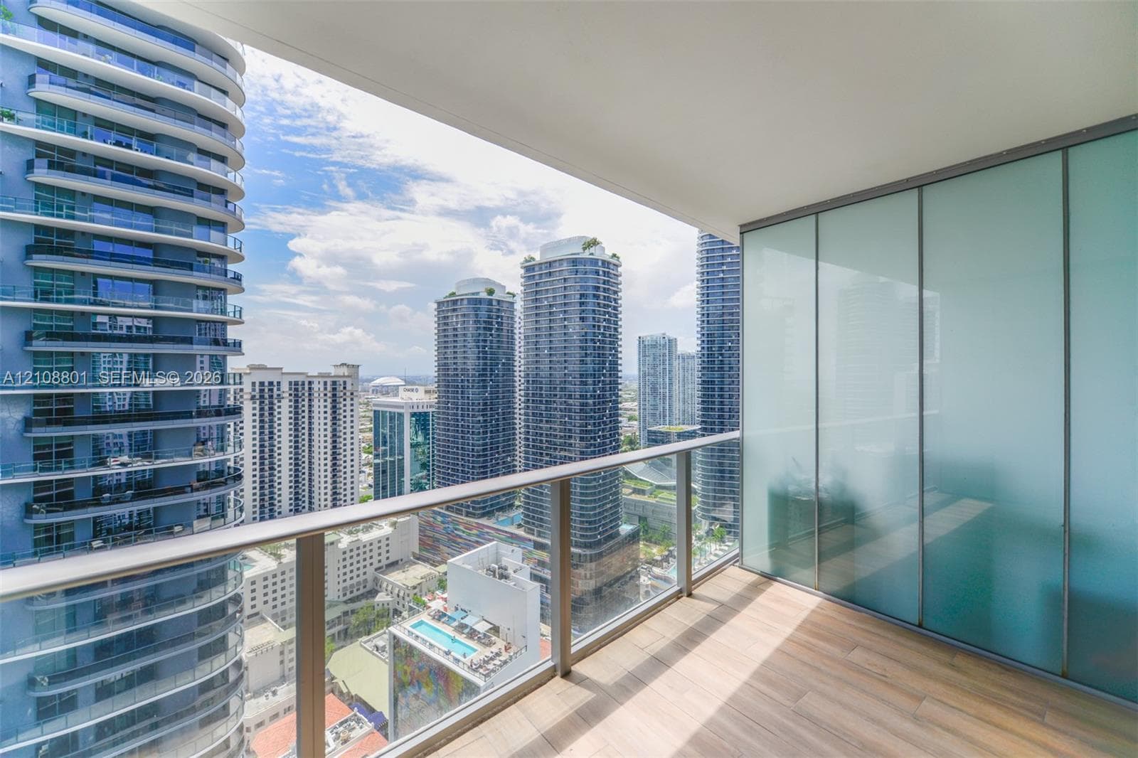 Private balcony featuring wood-finish flooring, glass panel railing, and frosted glass partition
