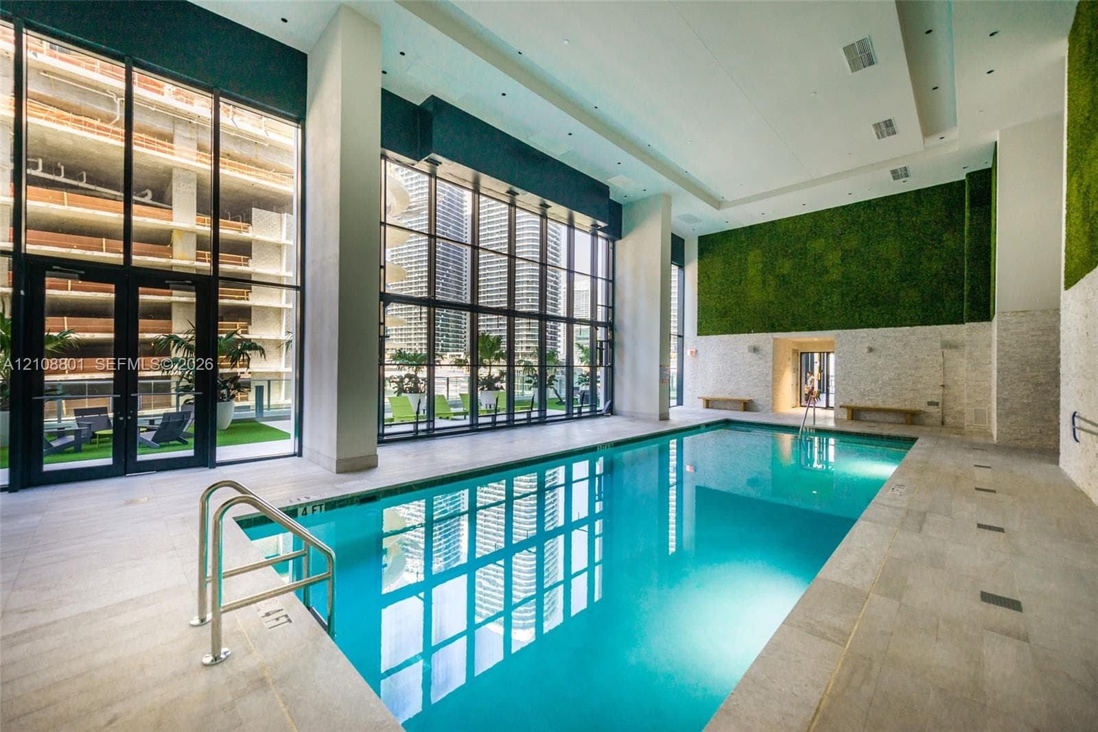 Indoor swimming pool featuring floor-to-ceiling glass walls, textured stone accent wall, integrated vertical greenery, and oversized tile flooring