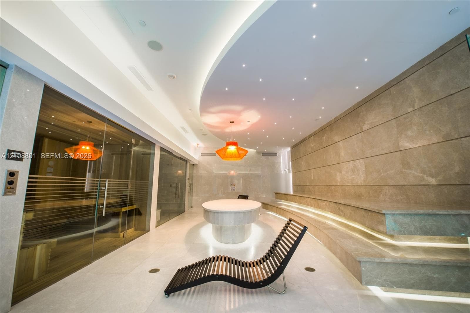 Spa room featuring a glass-enclosed sauna, tiered stone seating with under-step illumination, a curved ceiling with recessed lighting, and a stone-clad central pedestal