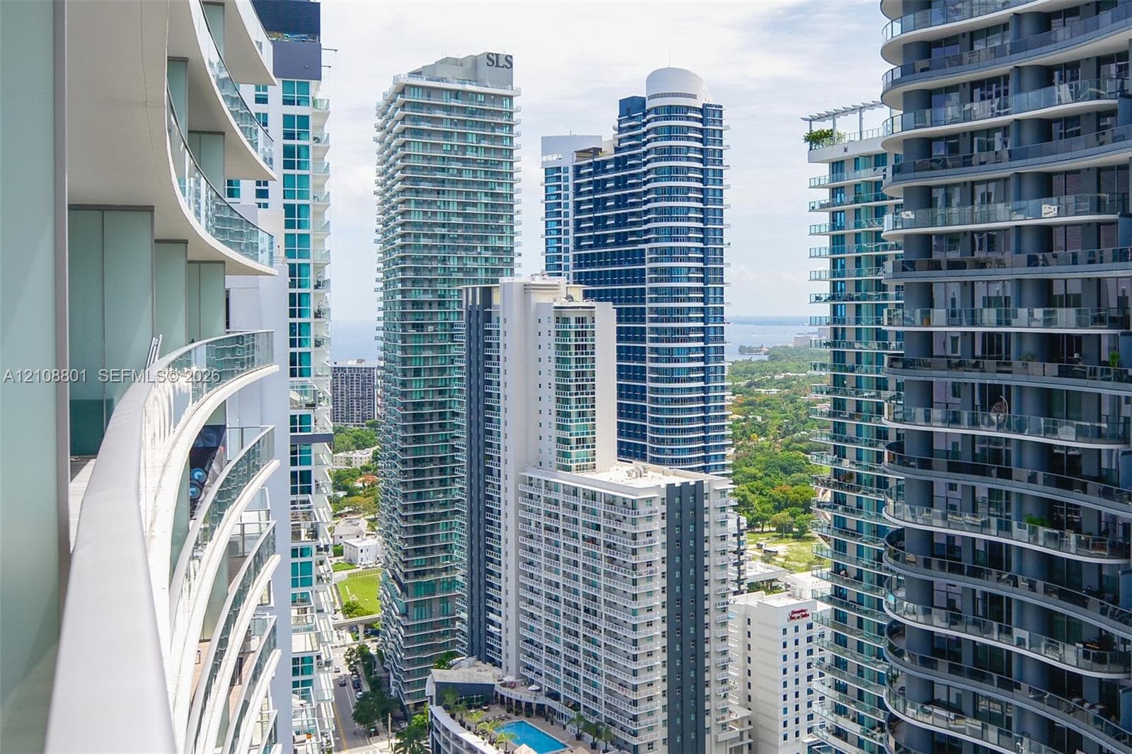 Curved exterior balcony with glass railing, high-rise architectural surroundings, and floor-to-ceiling glass elements