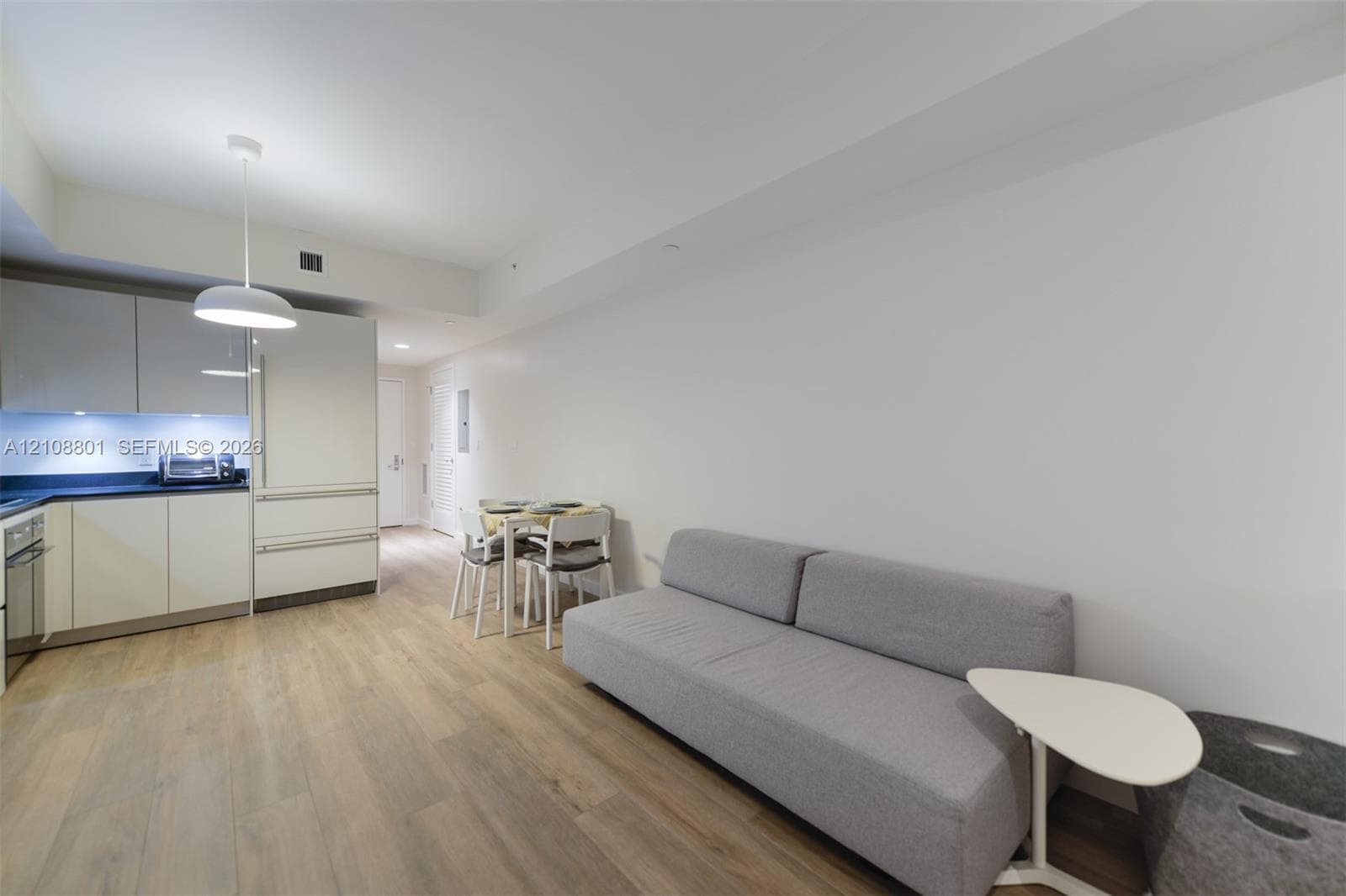 Kitchen featuring flat-panel cabinetry, dark solid-surface countertops, integrated stainless steel appliances, modern pendant lighting, and wood-finish flooring