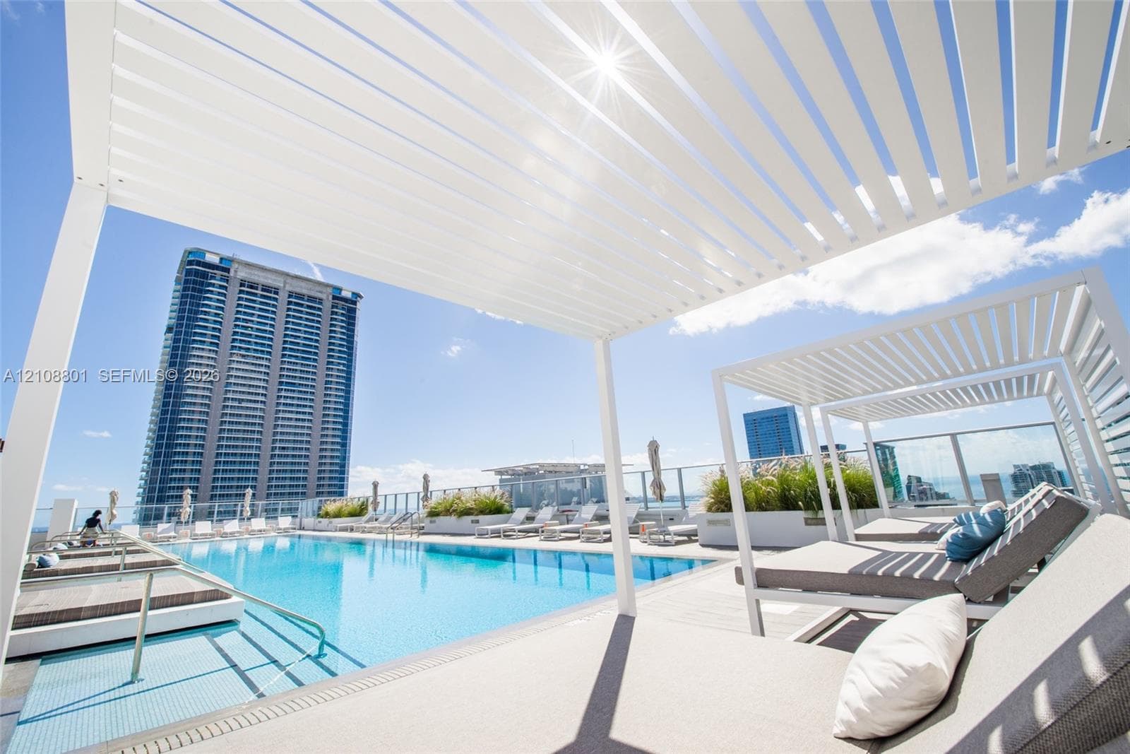 Rooftop pool featuring a tile finish, glass paneled railing, integrated wooden-finish decking, and white louvered pergolas