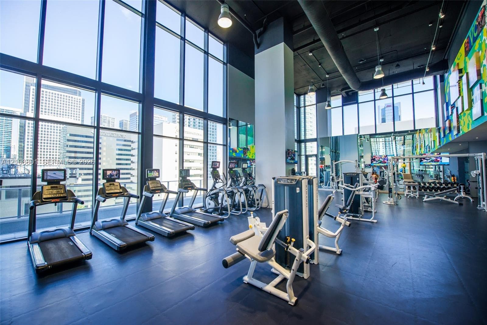 Fitness center featuring floor-to-ceiling windows, high ceilings with exposed ductwork, rubberized flooring, and built-in mirrored wall panels