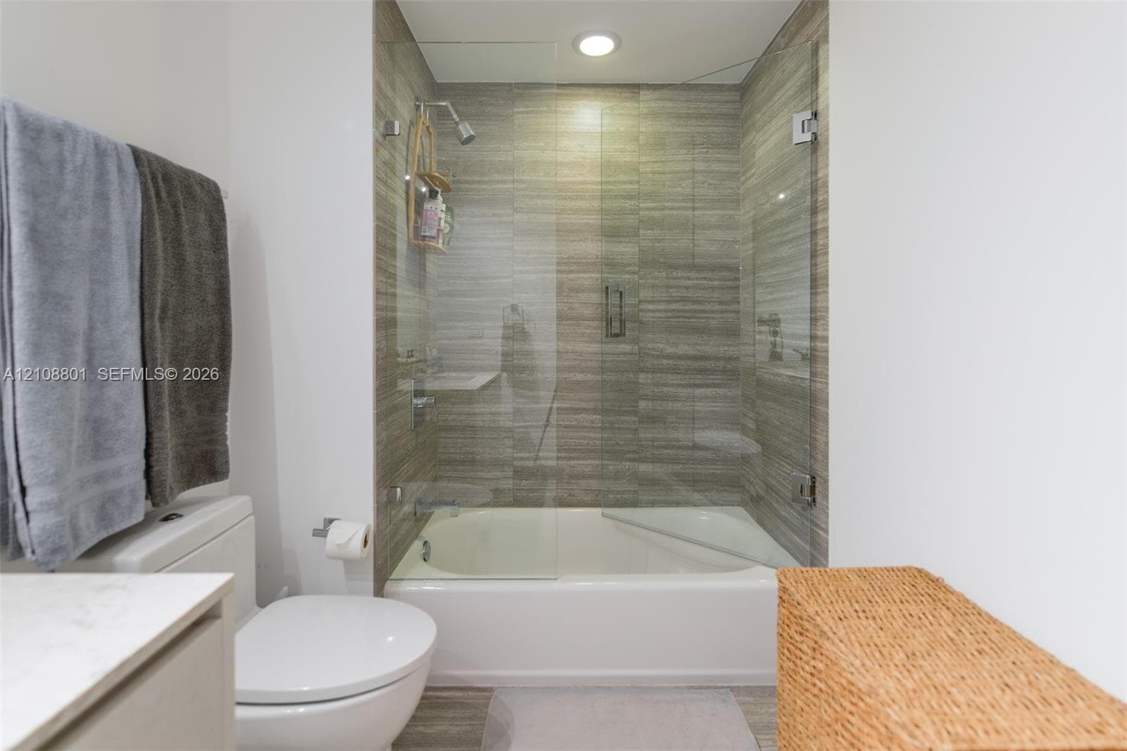 Full bathroom featuring a tub-shower combination with floor-to-ceiling tile surround and a frameless glass door, complemented by a stone-top vanity and low-profile toilet