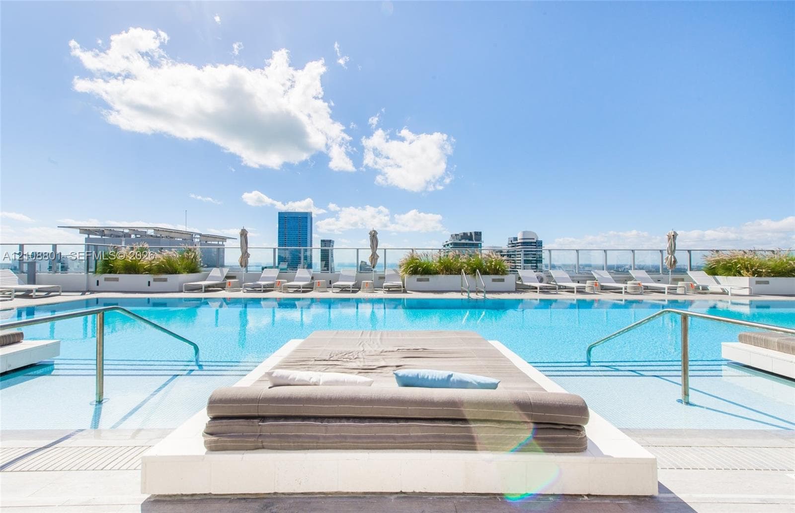 Rooftop swimming pool with integrated sun shelf, white stone tile decking, metal handrails, and glass perimeter railing