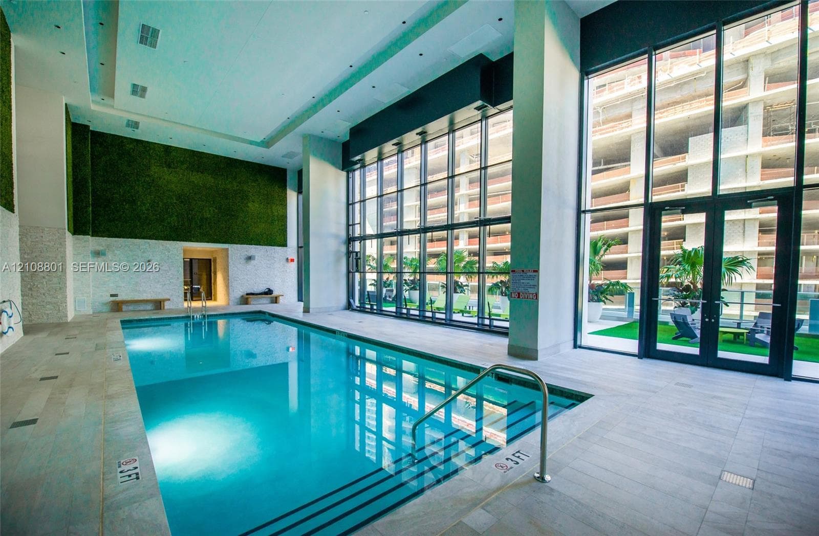 Indoor lap pool featuring floor-to-ceiling windows, stone tile flooring, high ceilings with recessed lighting, and a prominent decorative greenery wall
