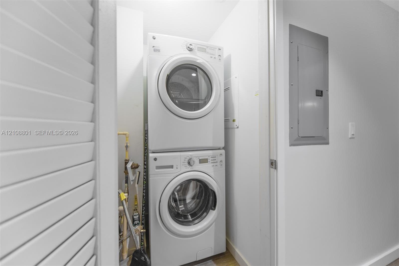 Laundry area featuring a stacked washer and dryer unit, louvered closet doors, and a wall-mounted electrical panel