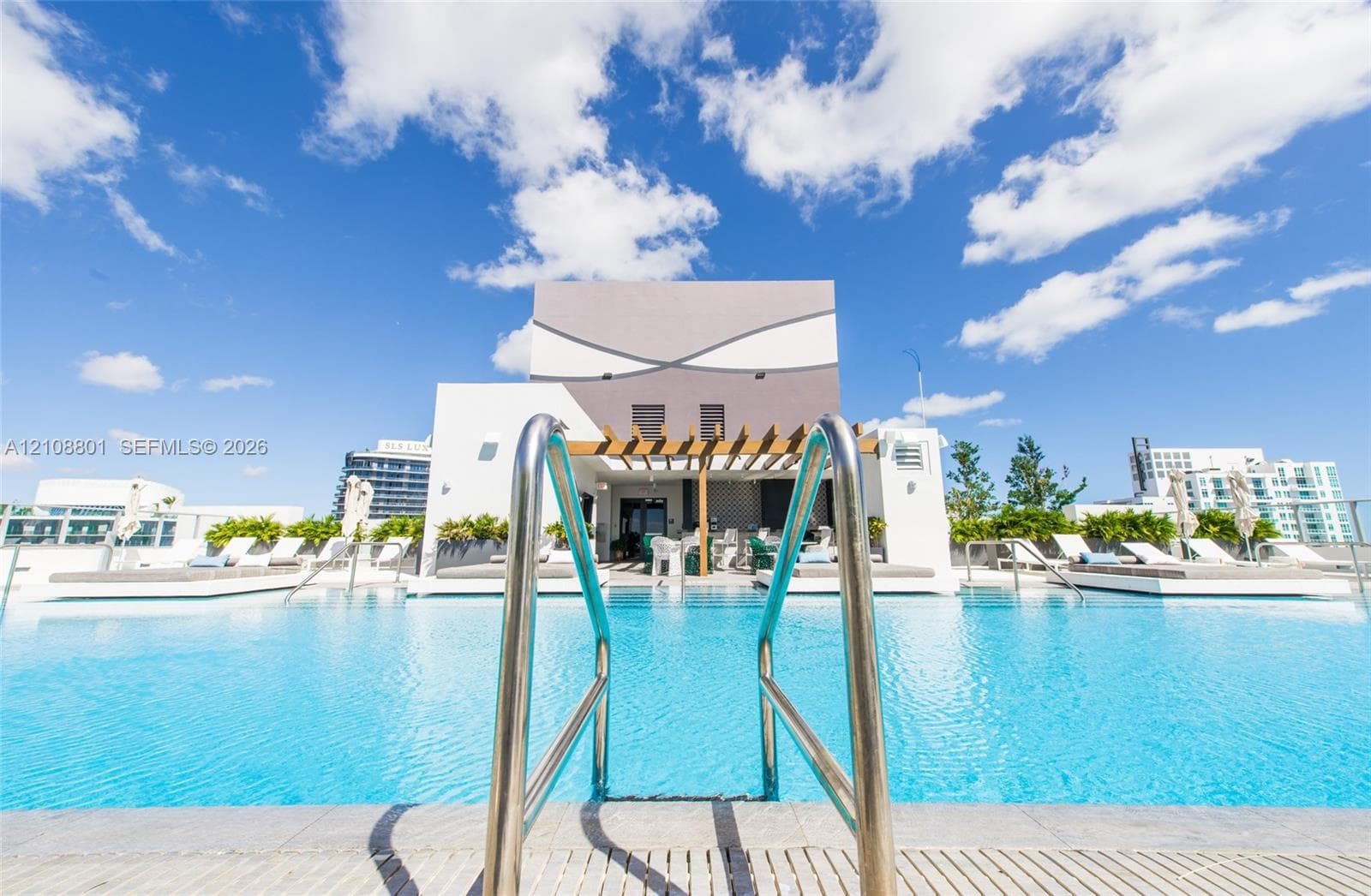 Rooftop swimming pool featuring metal handrails, a stone-tiled edge, and a wood-slatted pergola structure
