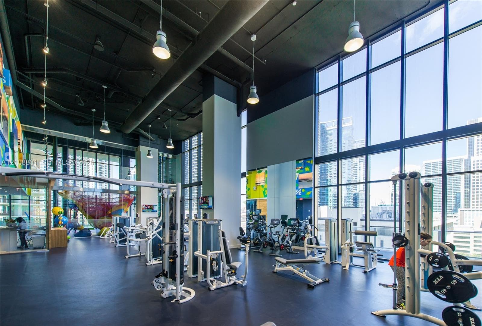 Fitness center featuring expansive floor-to-ceiling windows, high industrial-style ceilings, pendant lighting, and rubber flooring