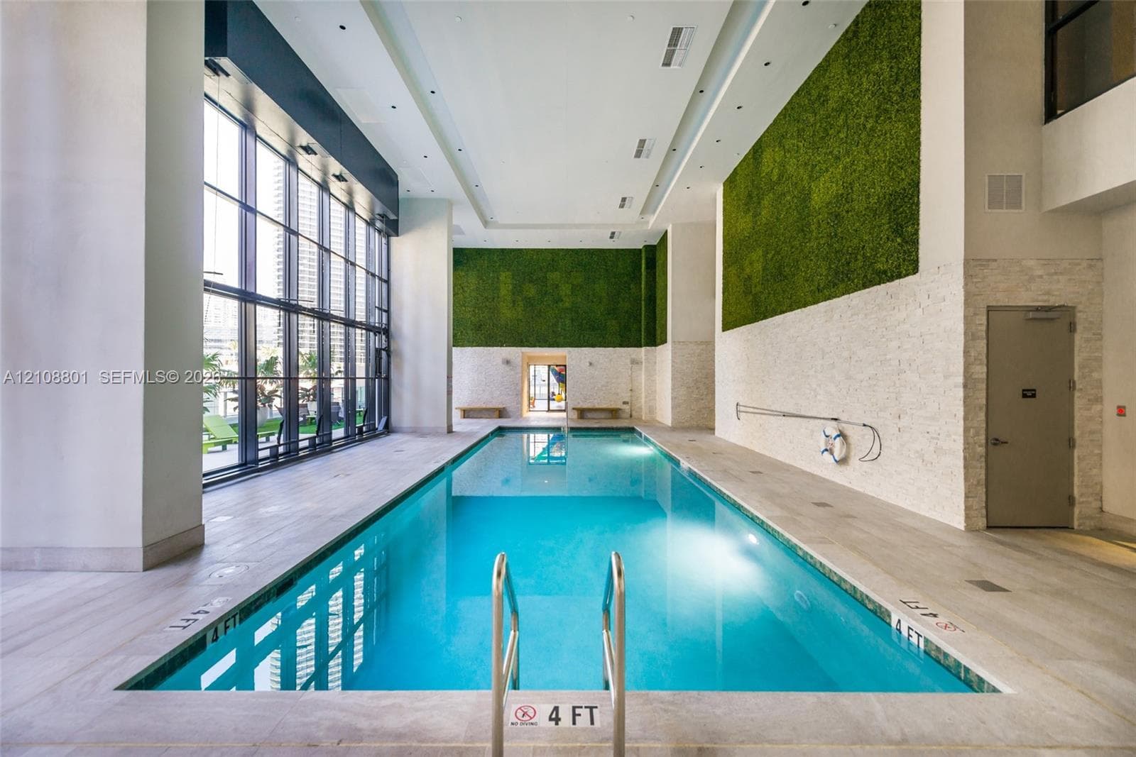 Indoor swimming pool featuring floor-to-ceiling windows, natural stone wall accents, decorative green wall installations, and recessed ceiling lighting