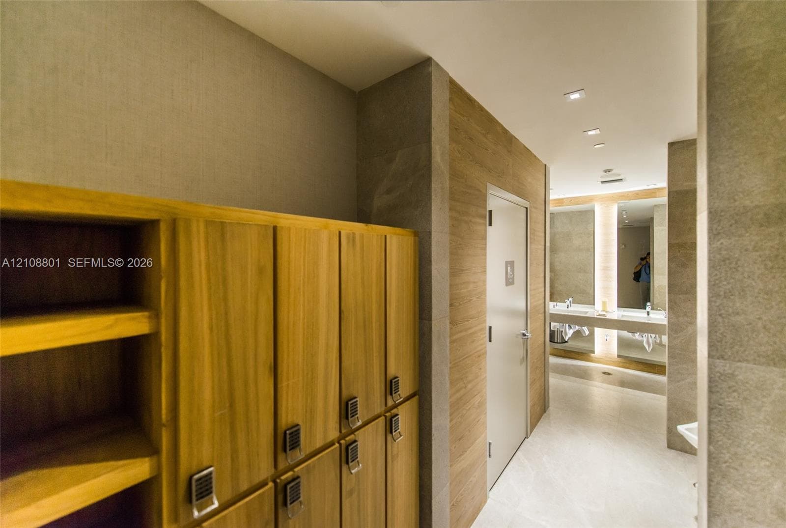 Custom wood-finish lockers with integrated keypads, stone wall cladding, recessed lighting, and a dual-sink vanity with full-length mirrors