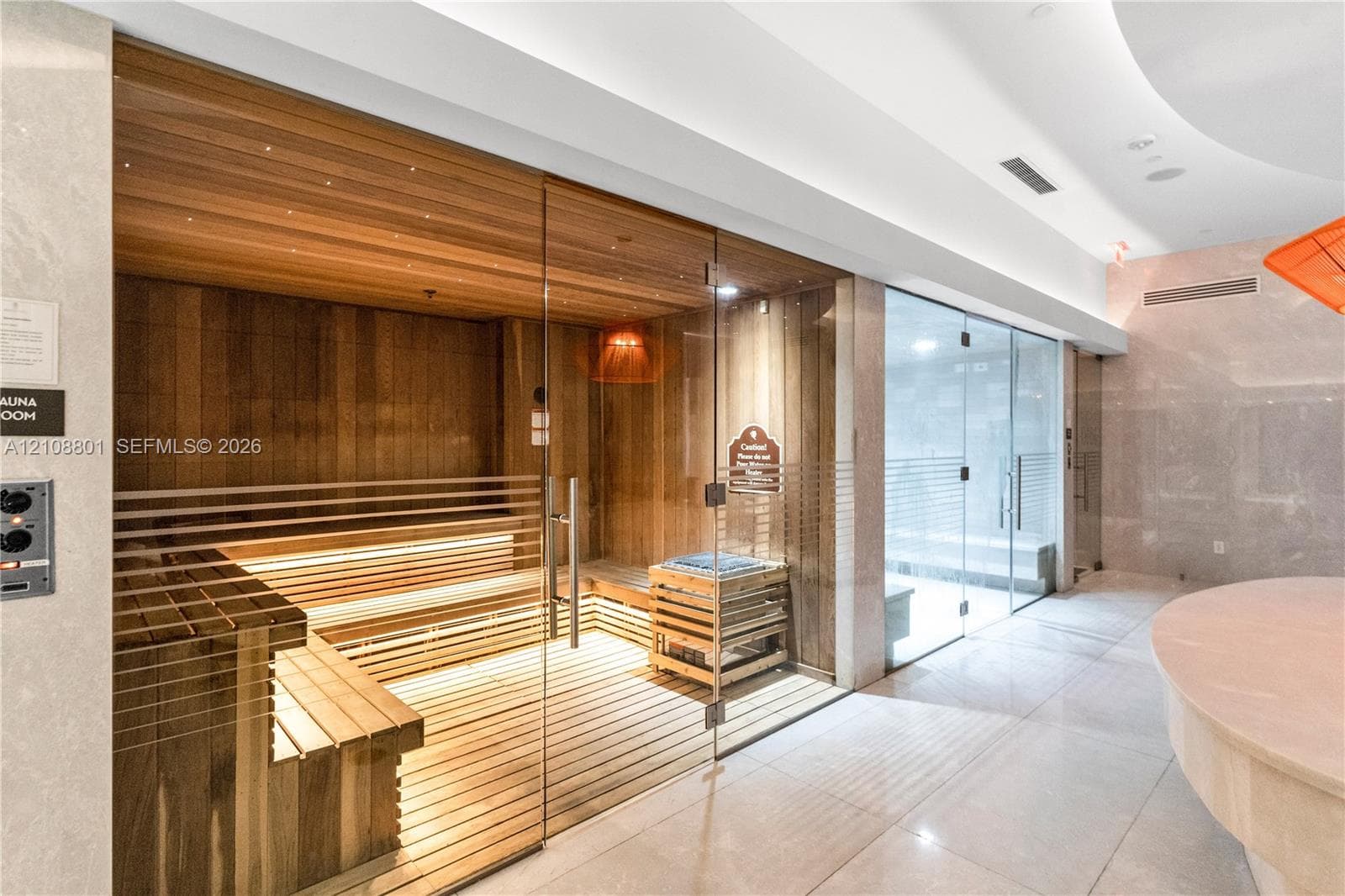 Sauna featuring natural wood-paneled walls and tiered bench seating, enclosed by a frameless glass door, accompanied by an additional glass-enclosed steam room and polished tile flooring