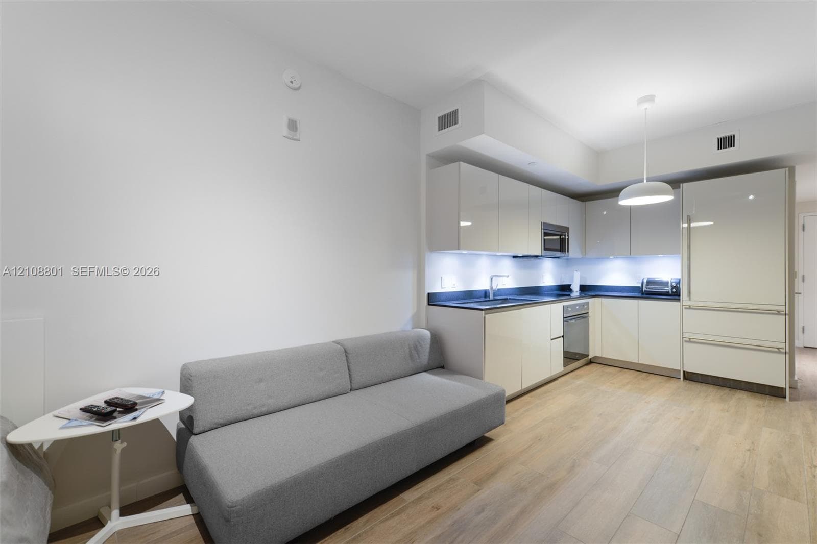 Modern kitchen featuring high-gloss cabinetry, dark solid-surface countertops, under-cabinet lighting, integrated appliances, and wood-finish flooring