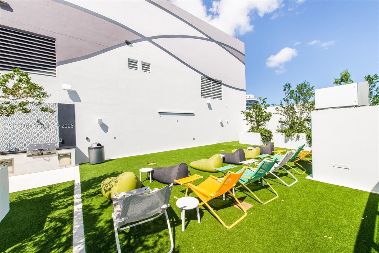 Outdoor terrace featuring artificial turf flooring, a built-in outdoor kitchen with patterned tile backsplash, and concrete planter walls