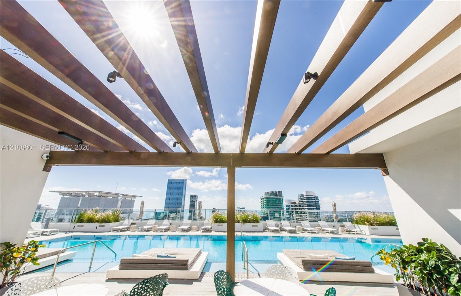 Rooftop swimming pool featuring a wooden pergola, integrated lighting, and perimeter glass railing with high-rise city scenery