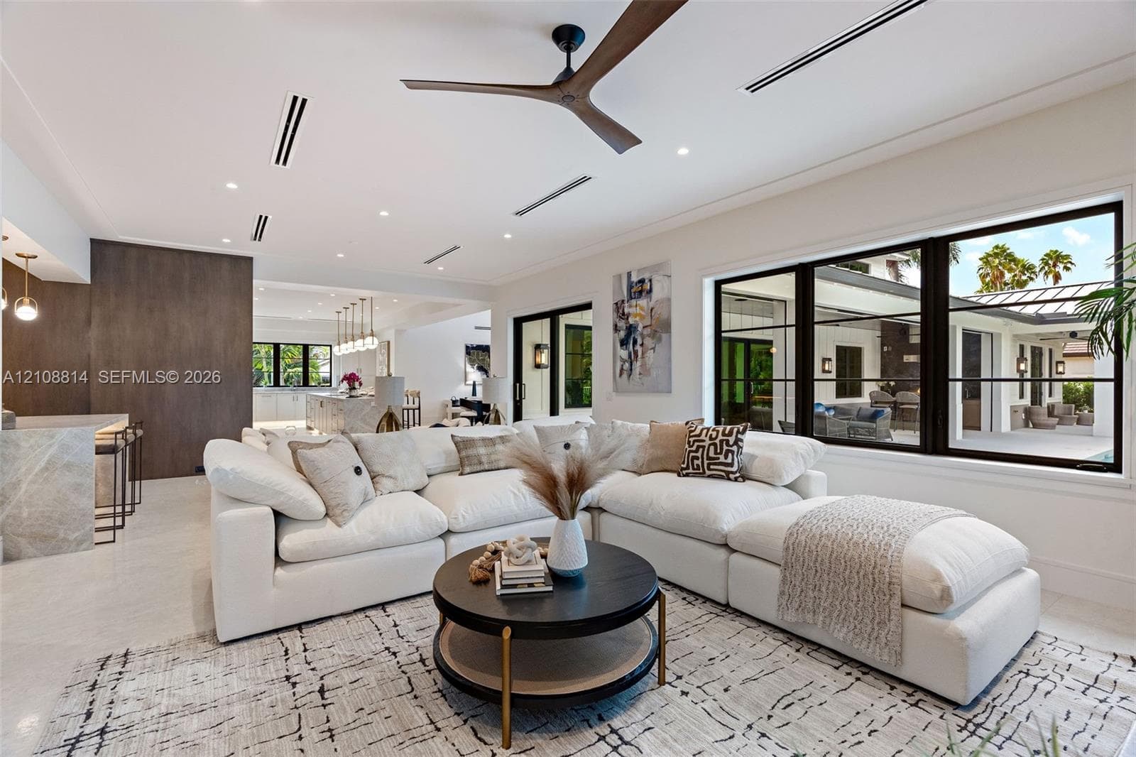 Open-concept living space featuring high ceilings with recessed lighting, a modern ceiling fan, expansive black-framed windows, and light-toned flooring