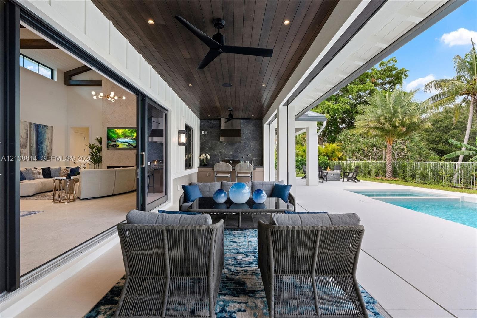Covered lanai featuring a wood-plank ceiling, recessed lighting, ceiling fans, integrated outdoor kitchen, and multi-panel sliding glass doors opening to a swimming pool and patio area