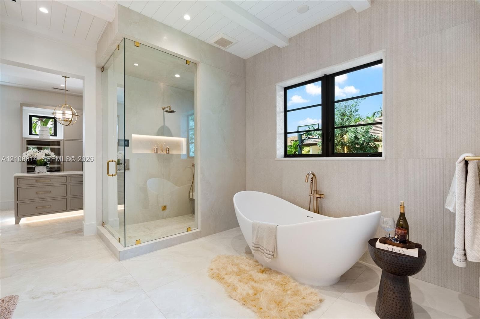 Freestanding soaking tub with a wall-mounted faucet, glass-enclosed shower featuring built-in shelving, large-format tile flooring, and plank-style ceiling detailing