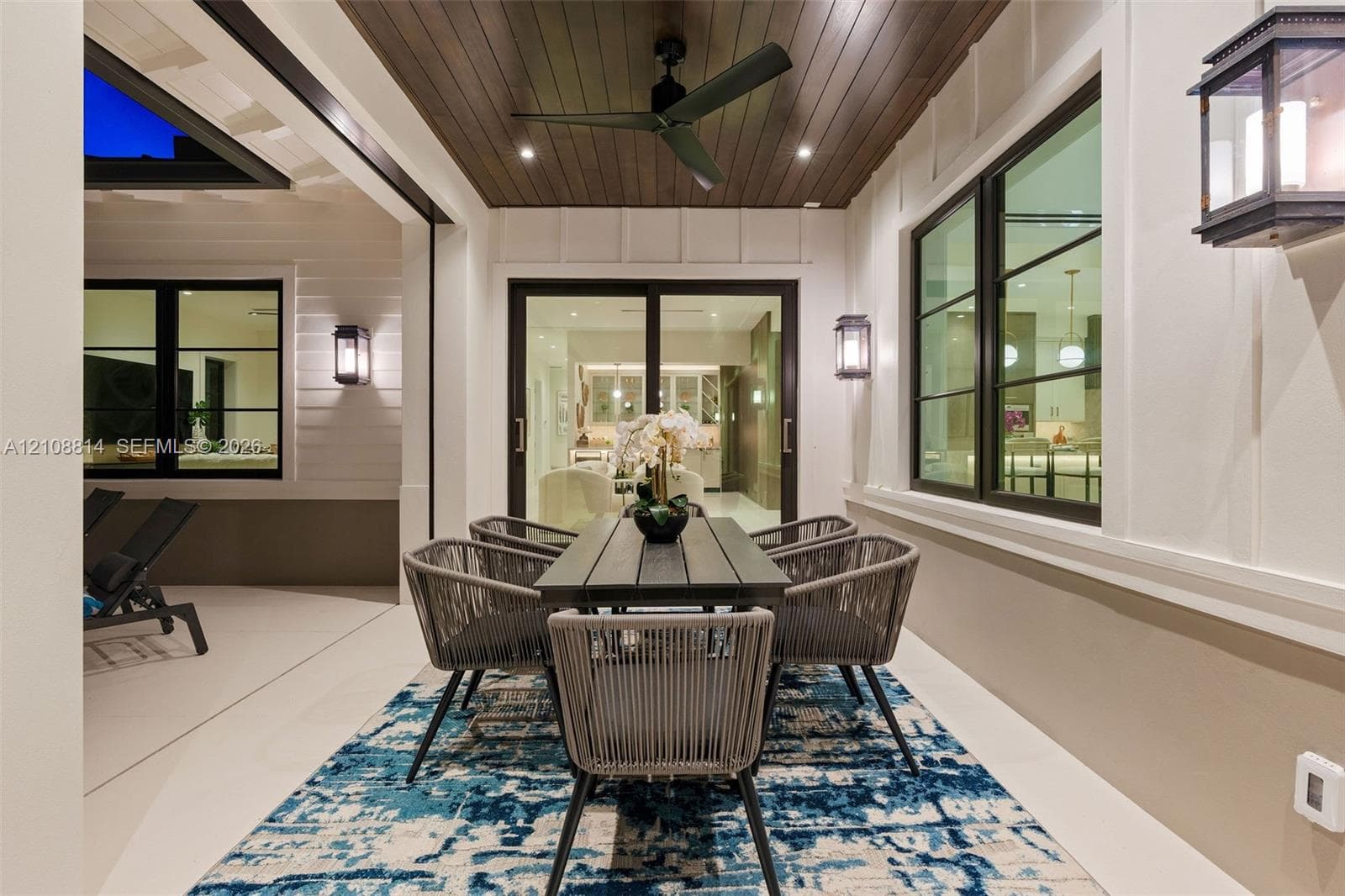 Covered patio featuring a wood-plank ceiling, matte black ceiling fan, recessed lighting, wall-mounted exterior lanterns, and multi-panel sliding glass doors