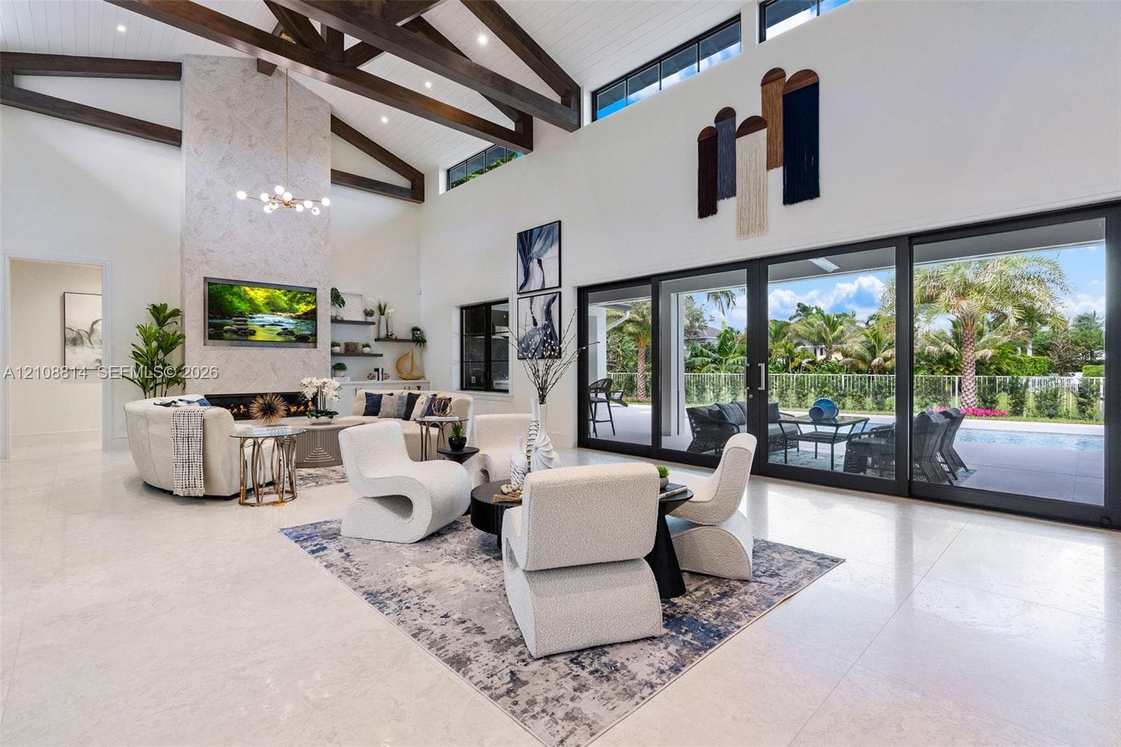 High-ceilinged living area featuring exposed wood ceiling beams, a floor-to-ceiling stone-clad fireplace, built-in shelving, and expansive multi-panel sliding glass doors