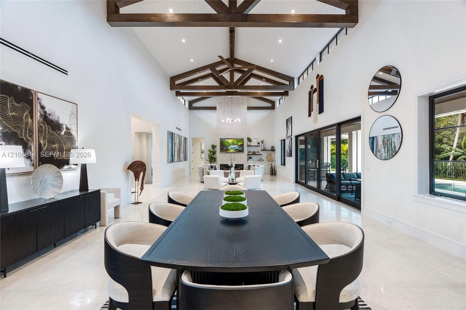 Vaulted ceilings with exposed wood beams, polished stone flooring, custom built-in cabinetry, floor-to-ceiling sliding glass doors, and a decorative tile fireplace surround