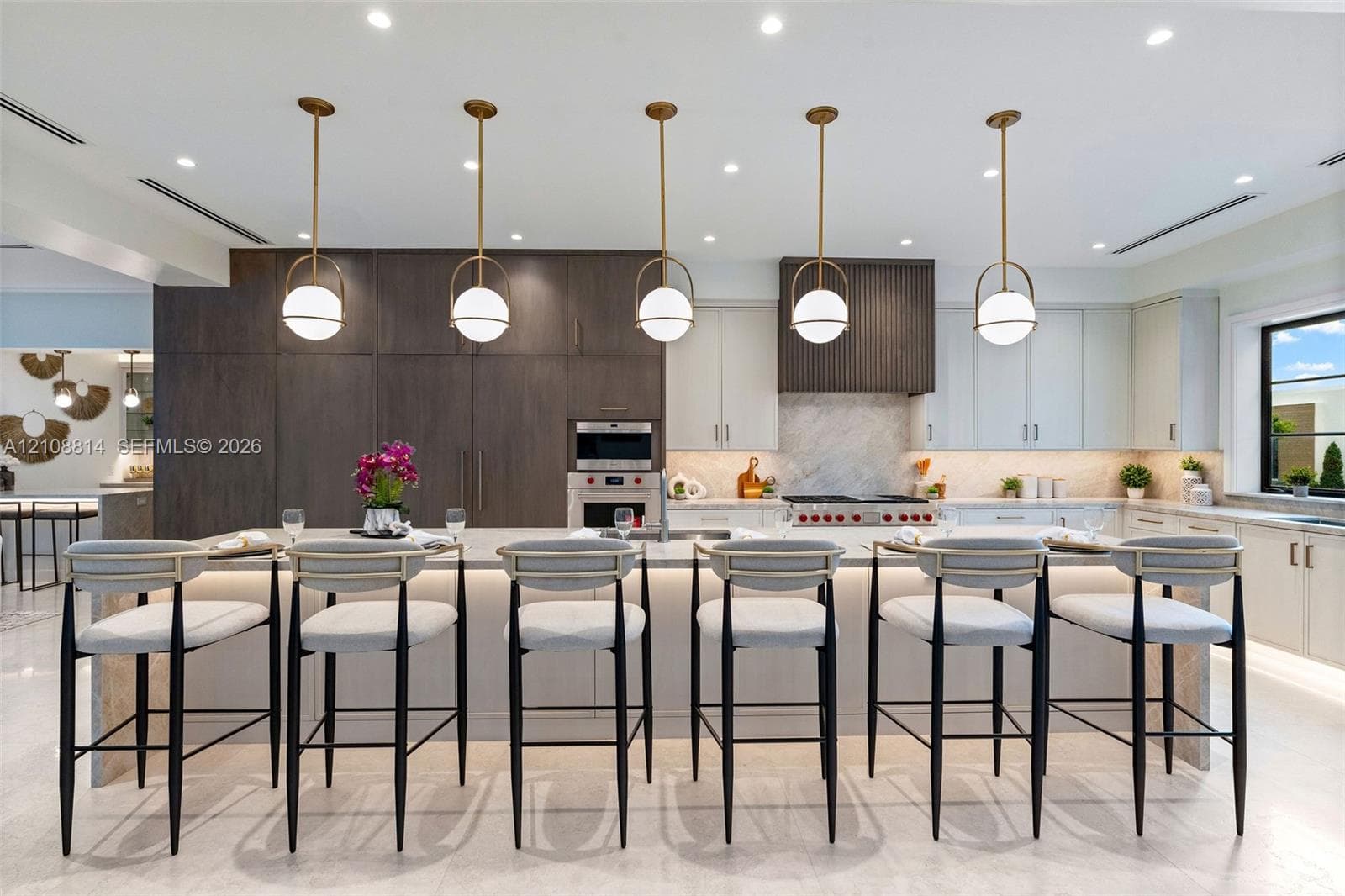 Kitchen featuring a large central island with waterfall-edge stone countertop, custom cabinetry, integrated professional-grade appliances, recessed lighting, and a series of globe-style pendant lights