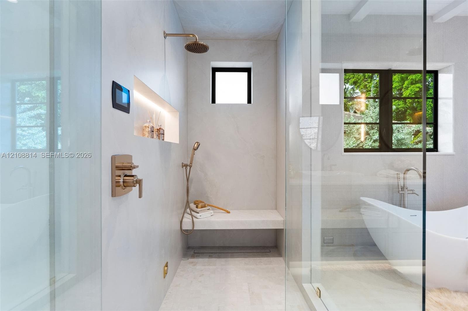 Walk-in shower featuring a built-in stone bench, rain showerhead with handheld sprayer, recessed shelving with integrated lighting, digital control interface, and floor-to-ceiling glass enclosure