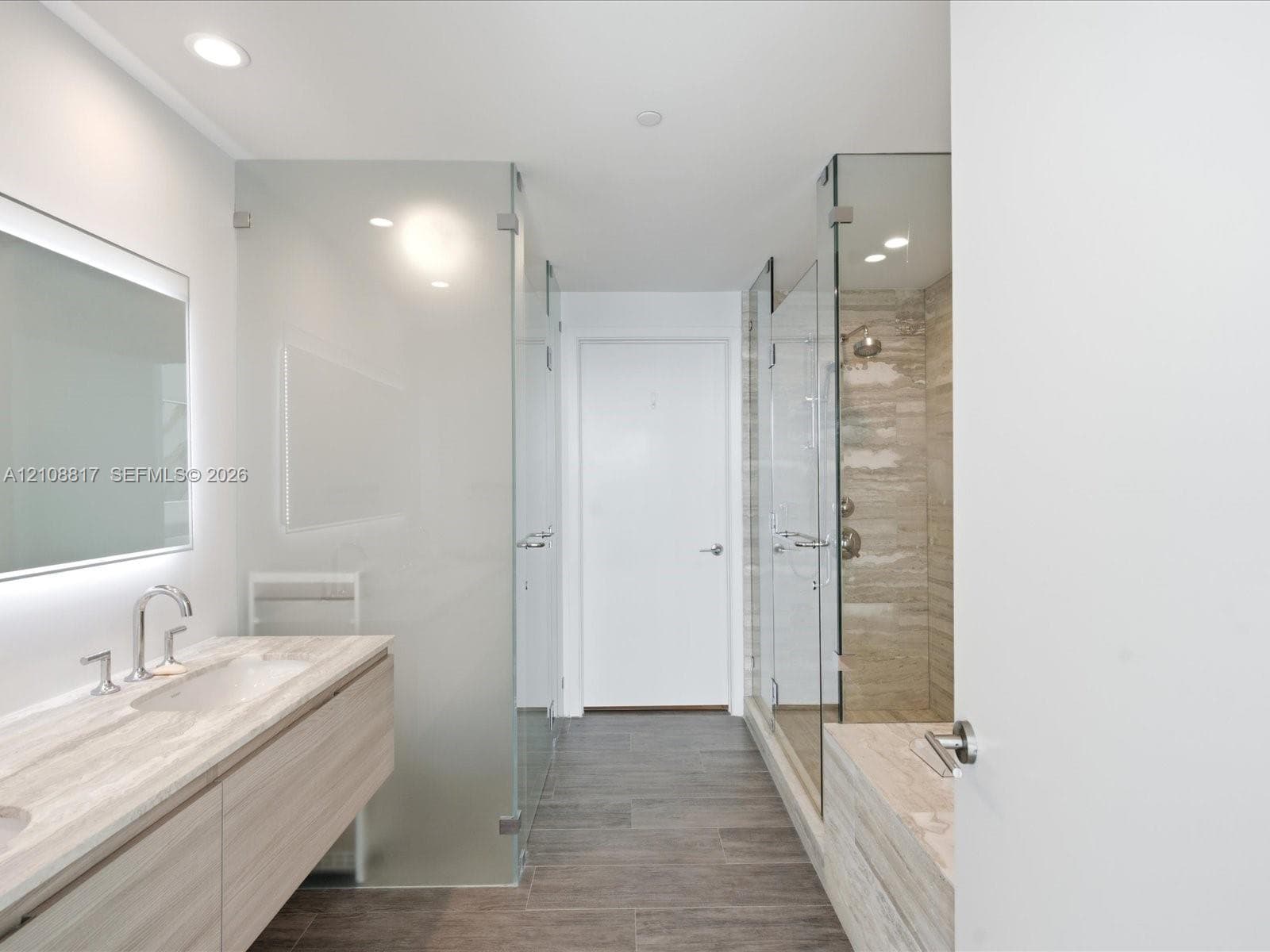 Floating vanity featuring a stone countertop and integrated sink, frameless glass shower enclosure with stone-tile surround, and wood-finish tile flooring