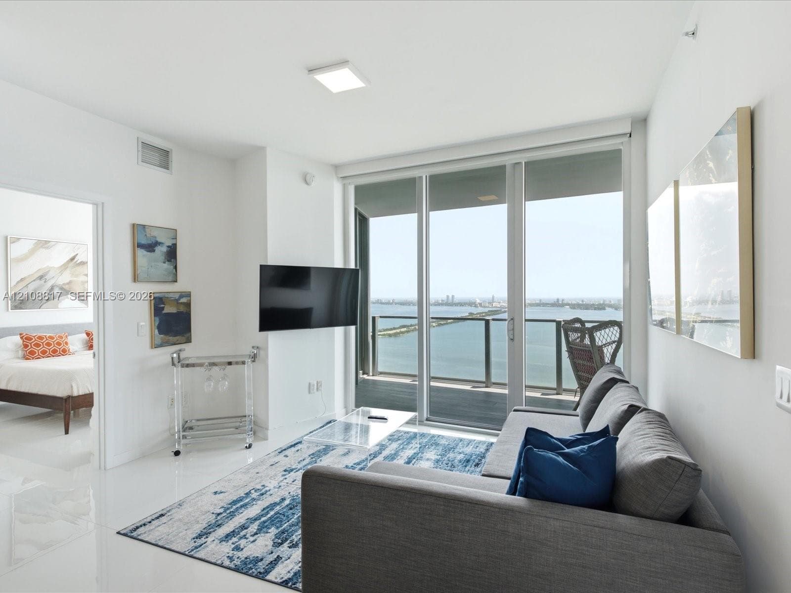 Floor-to-ceiling glass sliding doors with access to a private balcony, polished tile flooring, and panoramic water scenery