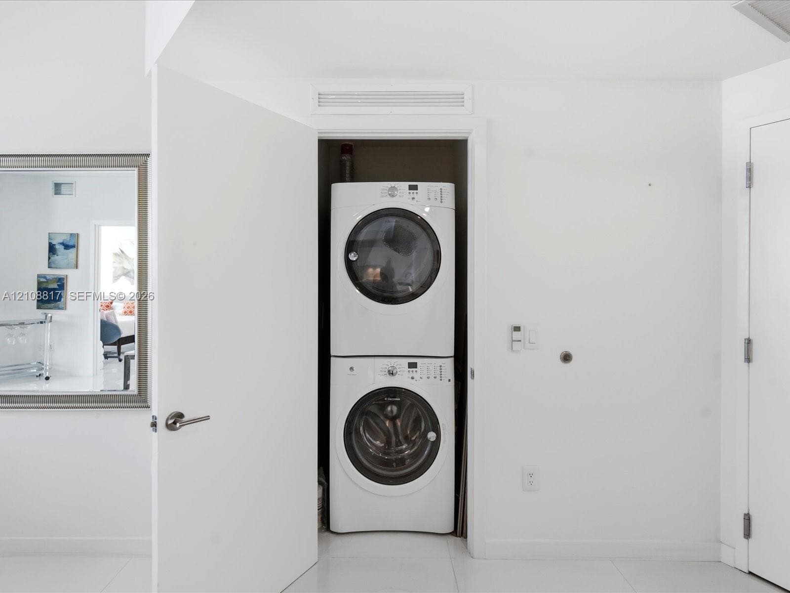 Stackable white front-load washer and dryer unit housed in a recessed closet