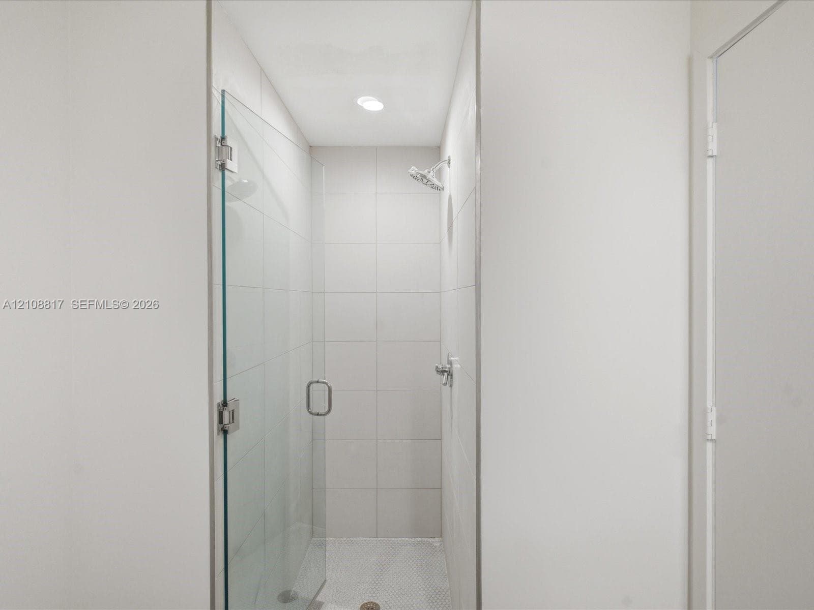 Walk-in shower featuring a frameless glass door, floor-to-ceiling white tile surround, mosaic tile flooring, and a chrome showerhead