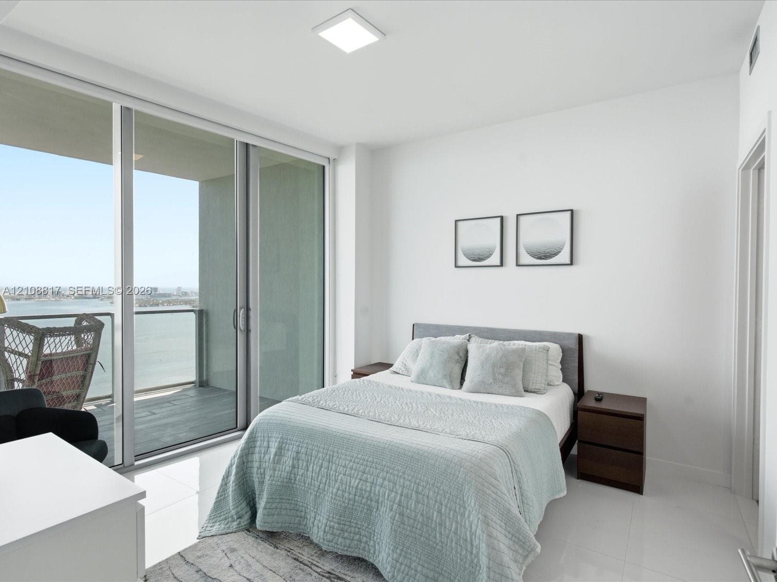 Floor-to-ceiling glass sliding doors opening to a private balcony, water scenery, and polished tile flooring
