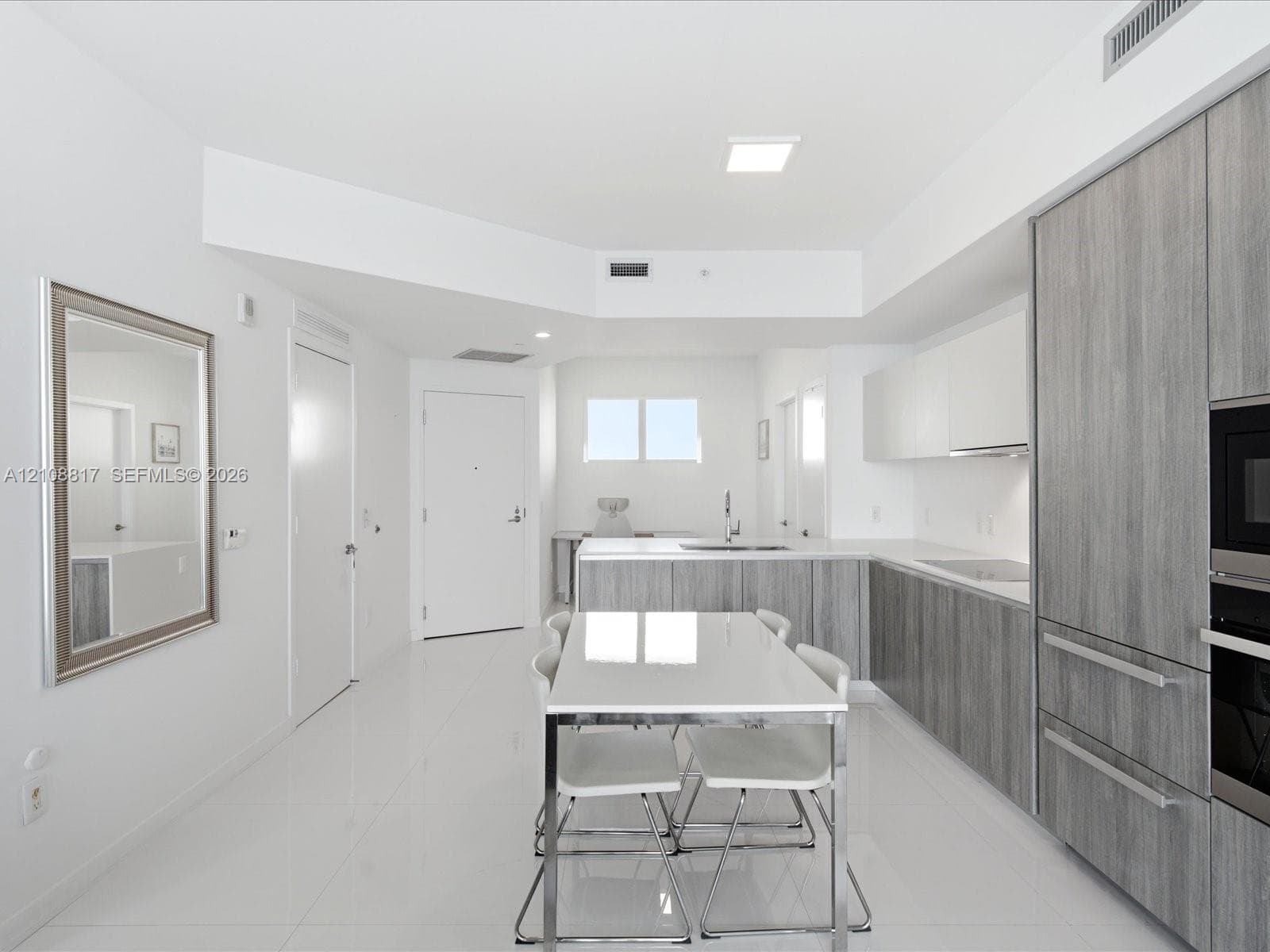 Modern kitchen featuring textured grey cabinetry, white solid-surface countertops, polished white flooring, and built-in stainless steel appliances