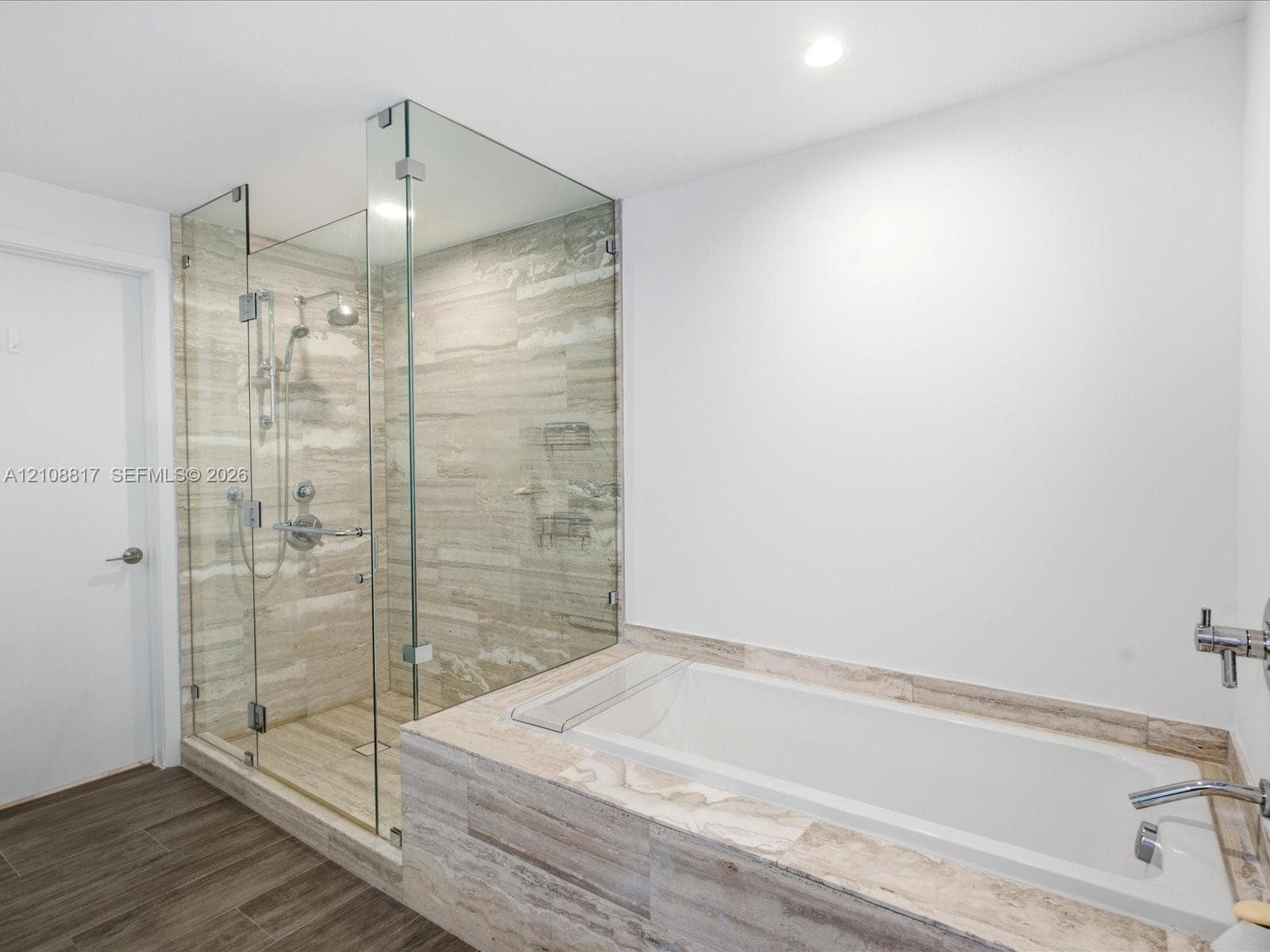 Walk-in glass-enclosed shower with a rainfall showerhead, alongside a built-in soaking tub featuring stone-finish tile surround and wood-finish flooring