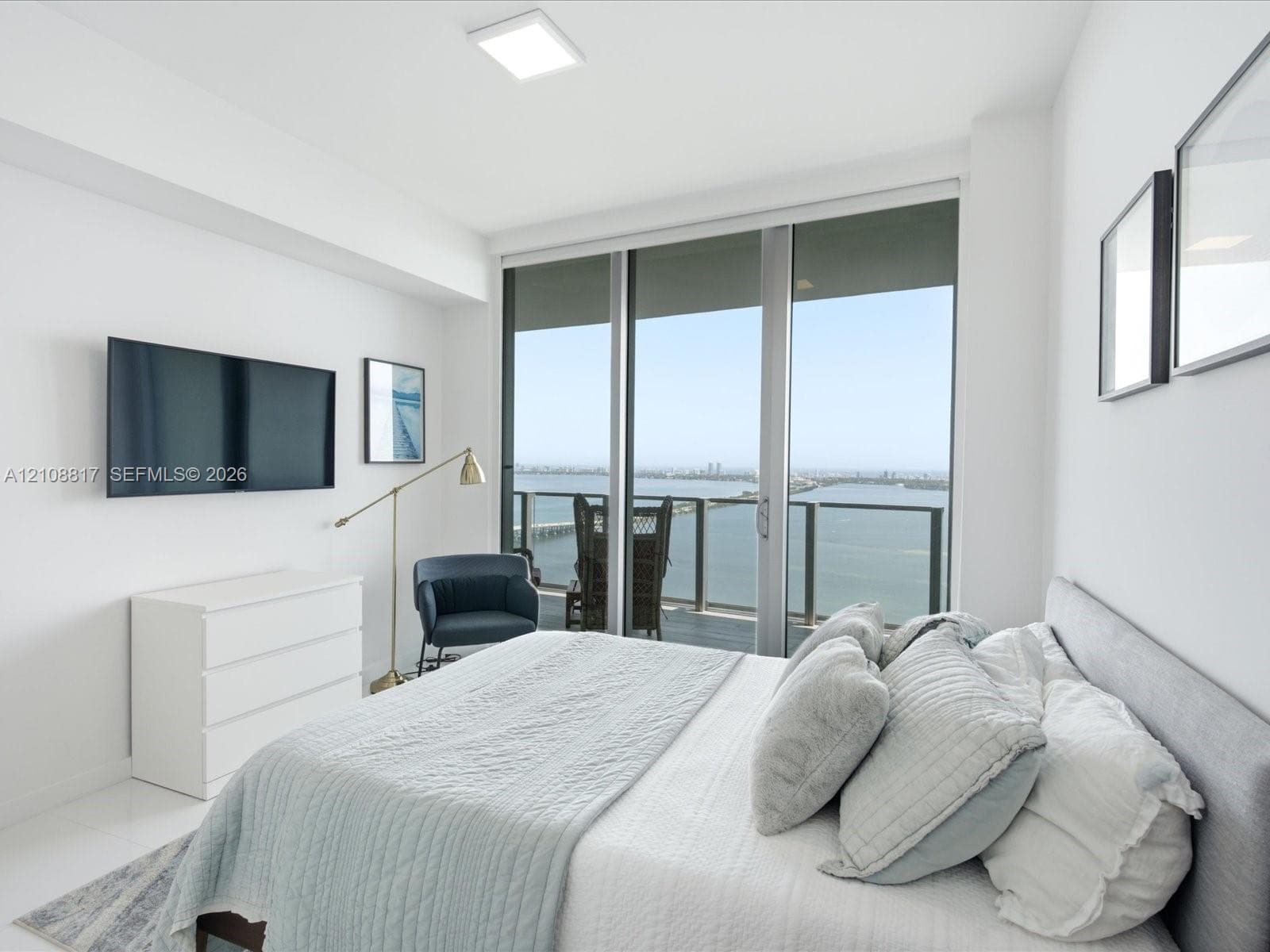 Floor-to-ceiling glass sliding doors opening to a private balcony, polished white tile flooring, and water scenery