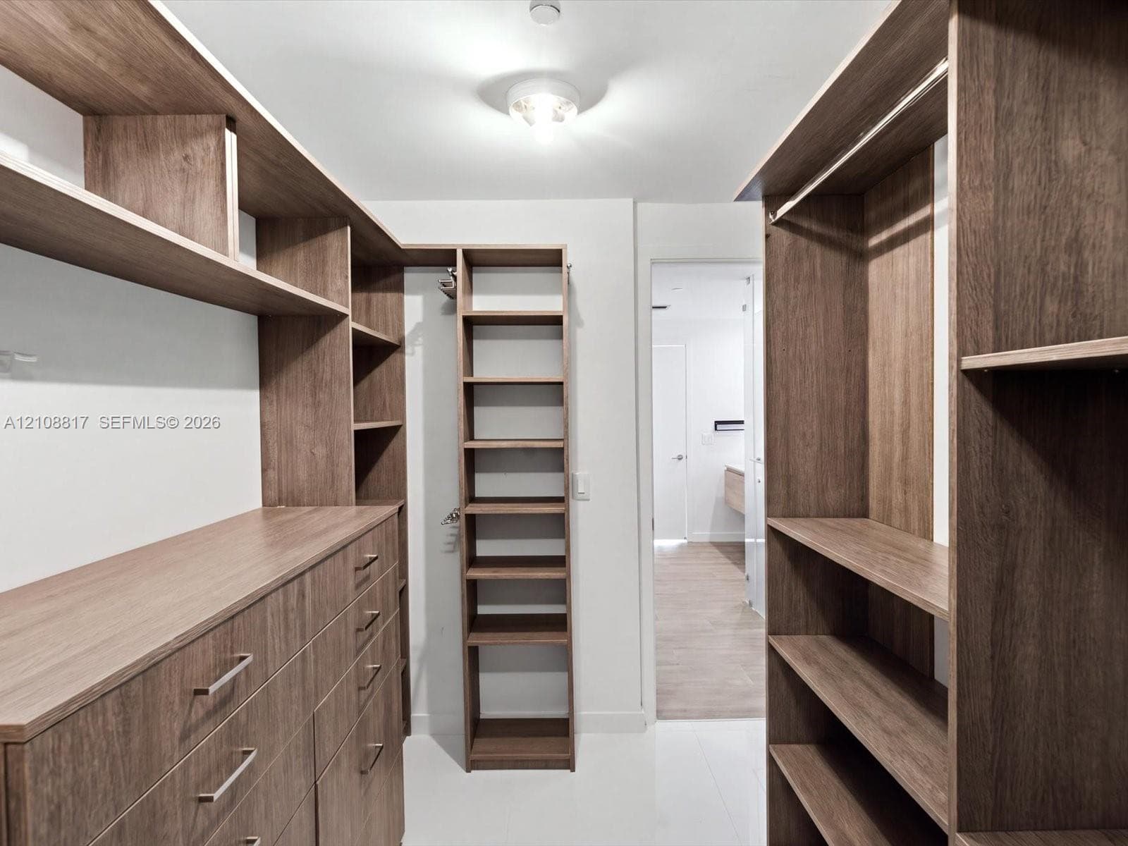 Walk-in closet featuring custom wood-finish cabinetry, floor-to-ceiling shelving, integrated drawer banks, and brushed metal hardware