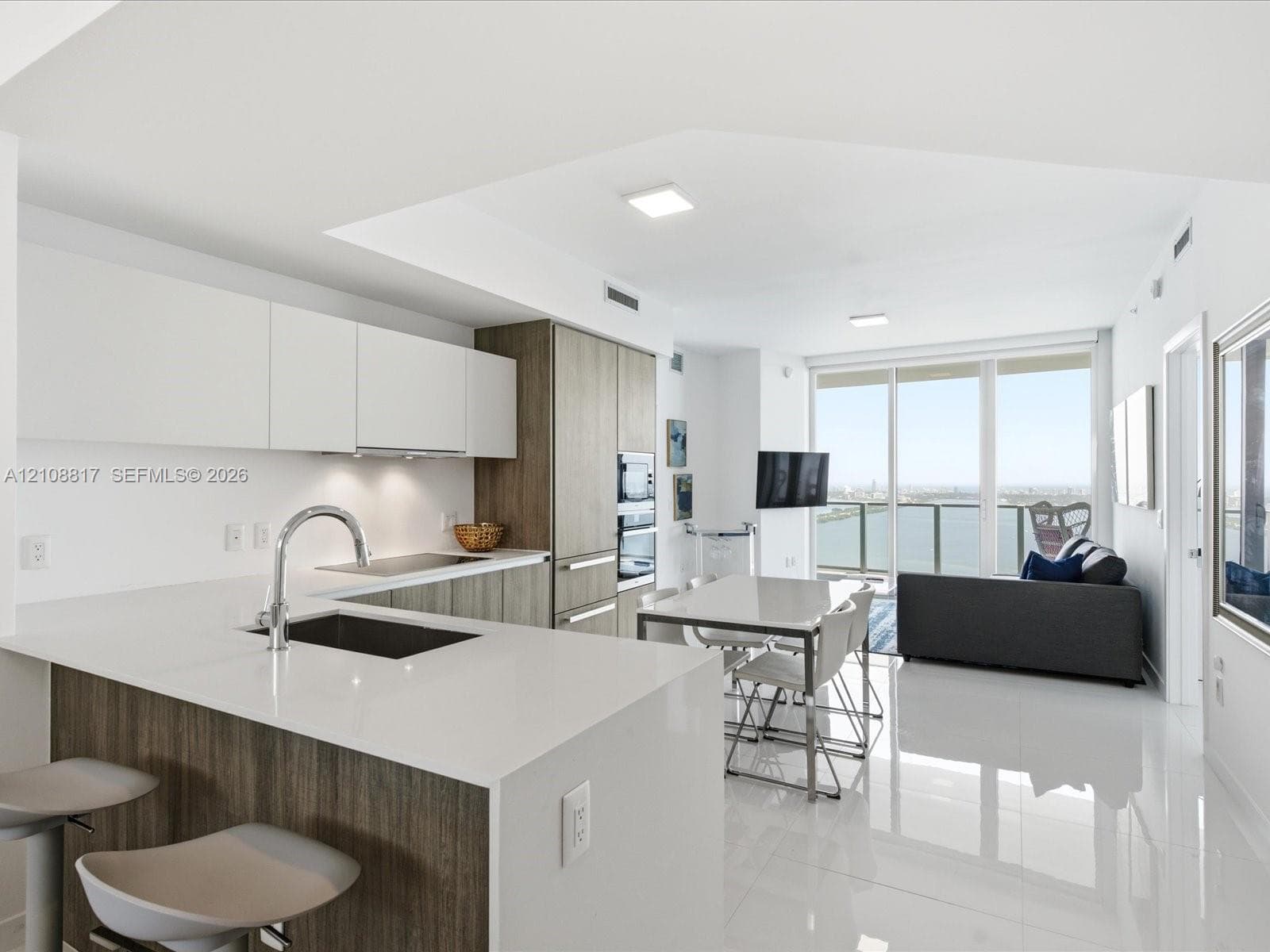 Kitchen featuring matte white cabinetry, wood-finish lower cabinetry, quartz countertops, integrated stainless steel appliances, and large-format tile flooring