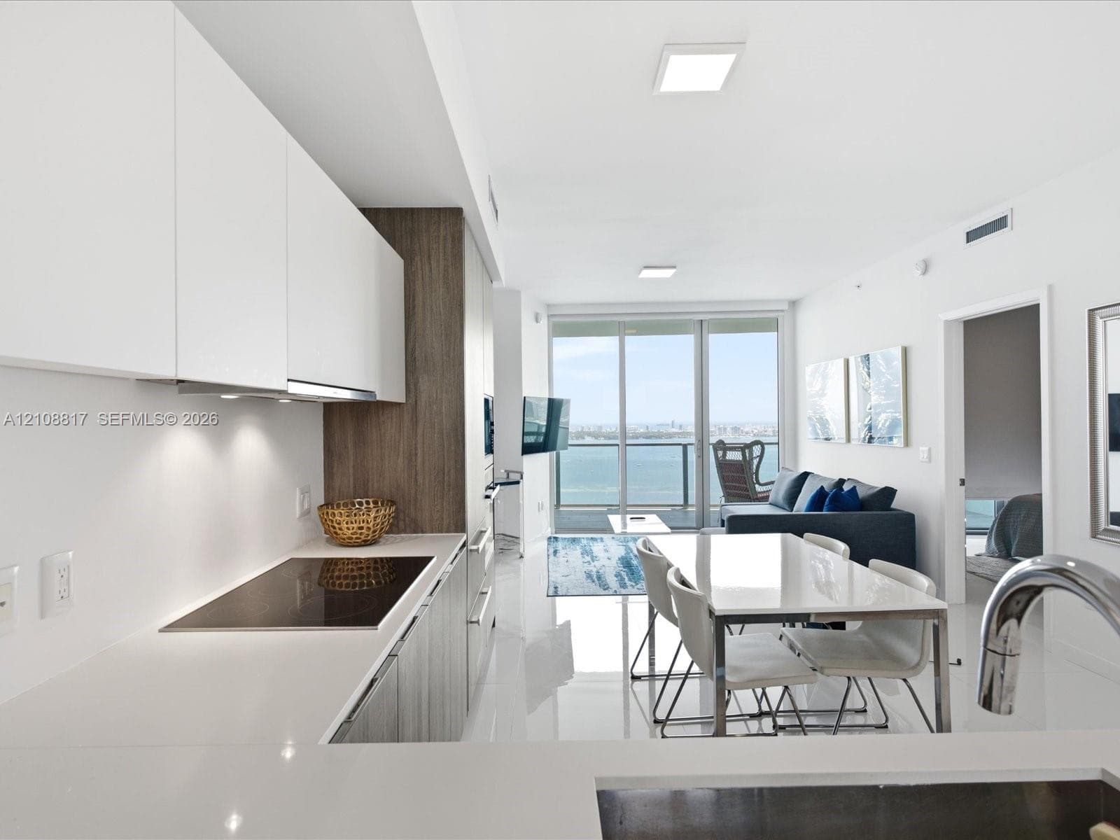 Modern kitchen featuring flat-panel cabinetry, light-toned countertops, built-in cooktop, and large-format tile flooring, accented by floor-to-ceiling glass doors opening to a balcony