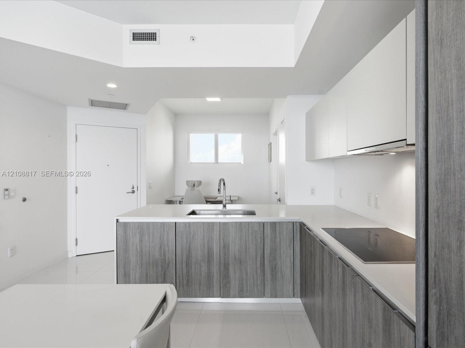 Modern kitchen featuring flat-panel cabinetry with wood-finish lower cupboards, solid surface countertops, an undermount sink with a gooseneck faucet, and an integrated induction cooktop