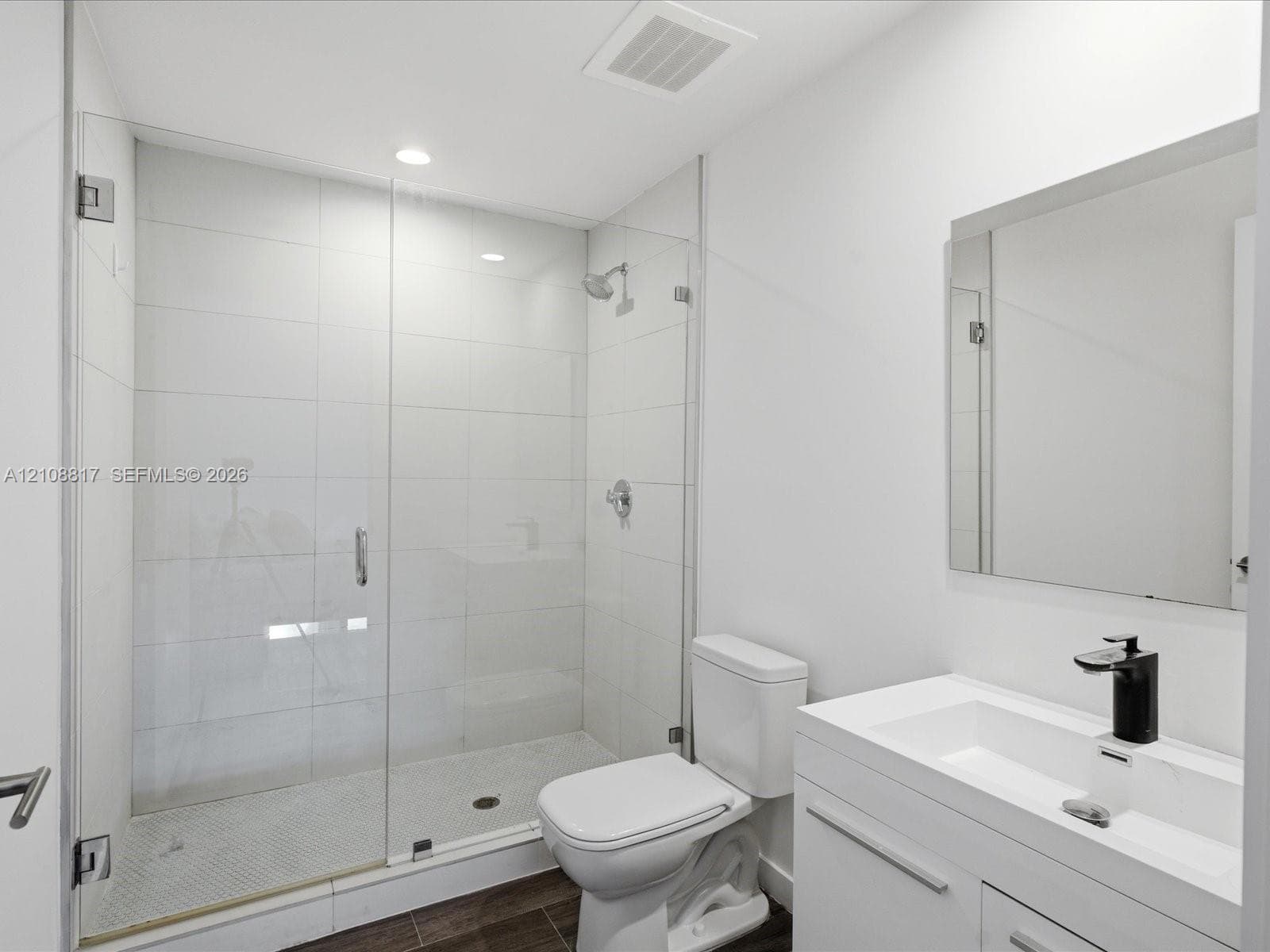 Walk-in shower with a glass enclosure, floor-to-ceiling white tile, modern vanity with a rectangular sink, matte black faucet, and polished mirror