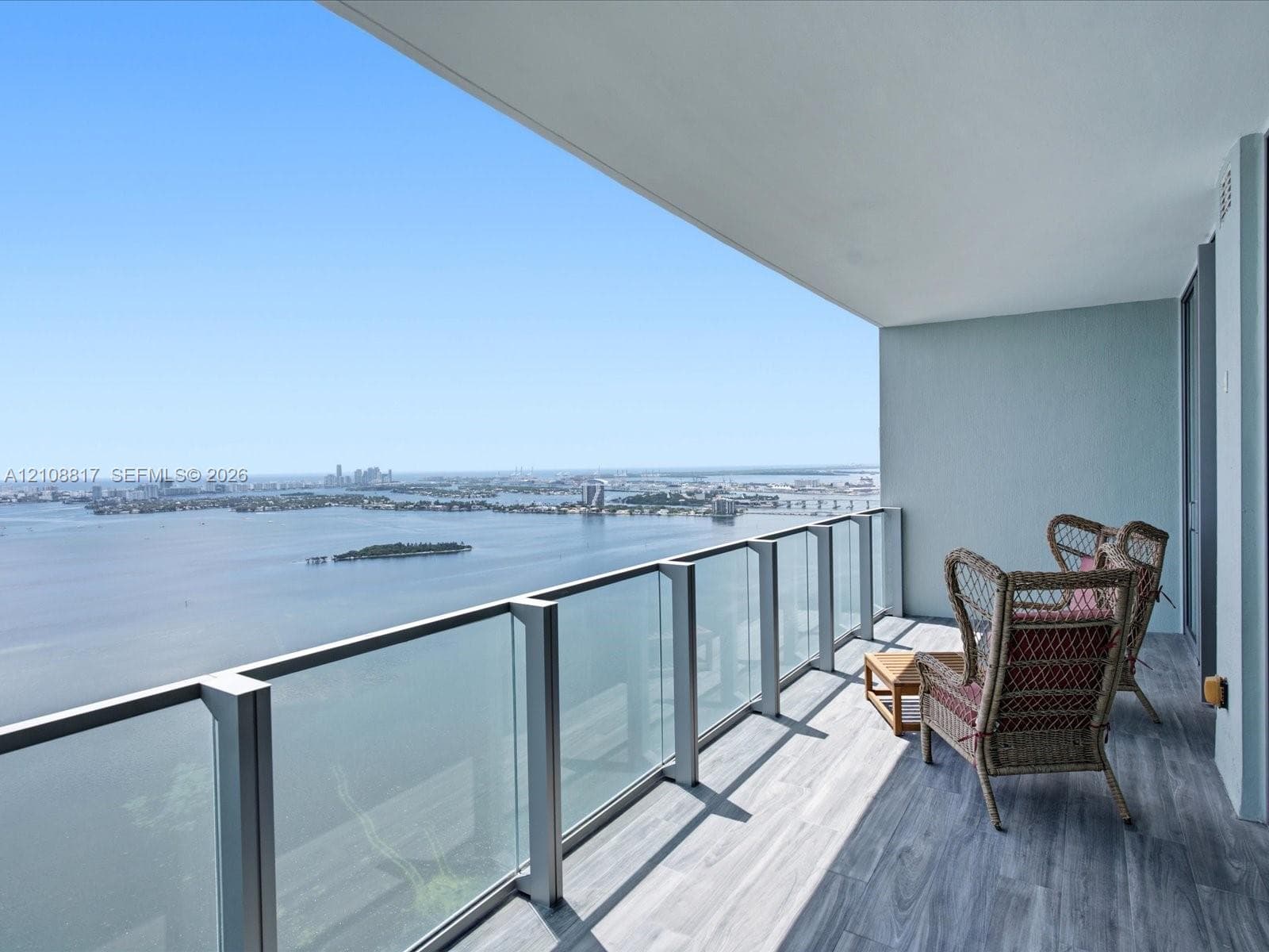 Covered balcony featuring wood-finish flooring and glass-paneled railing with metal framing, overlooking a wide expanse of water