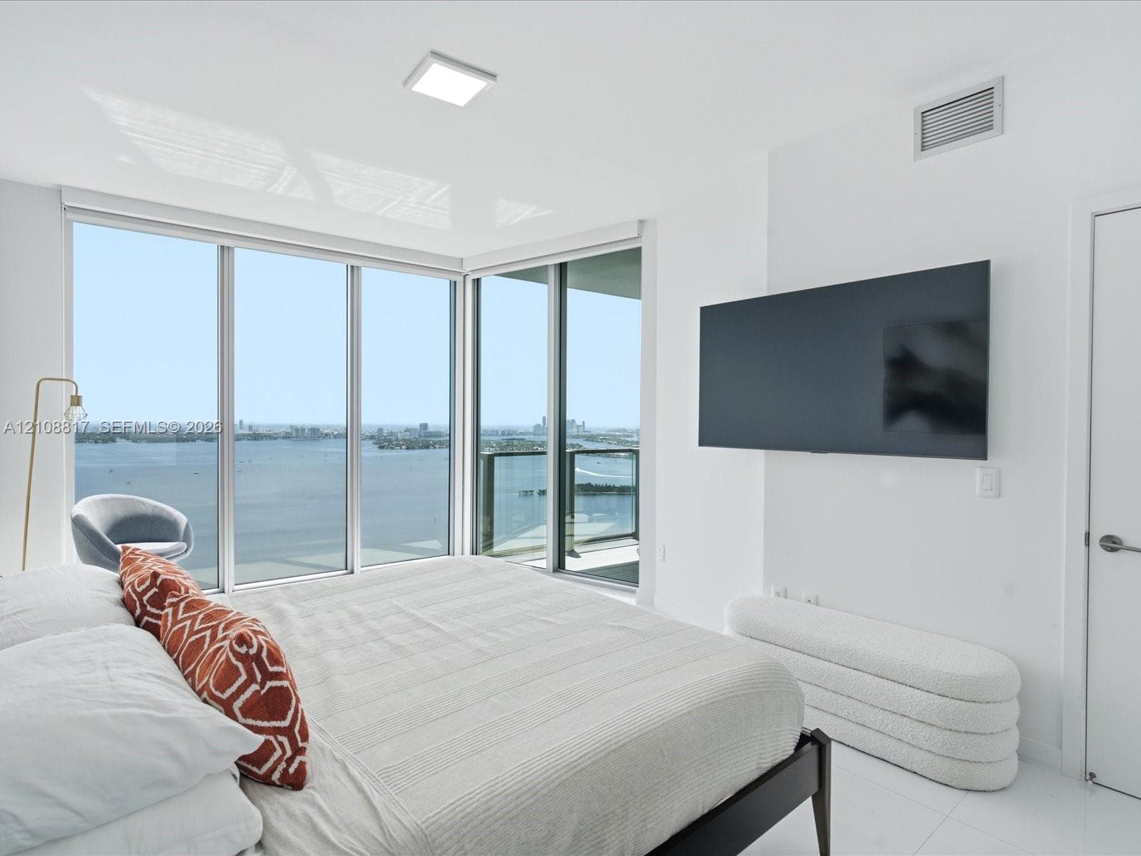 Floor-to-ceiling corner windows, expansive water backdrop, private glass-railed balcony, and recessed ceiling lighting