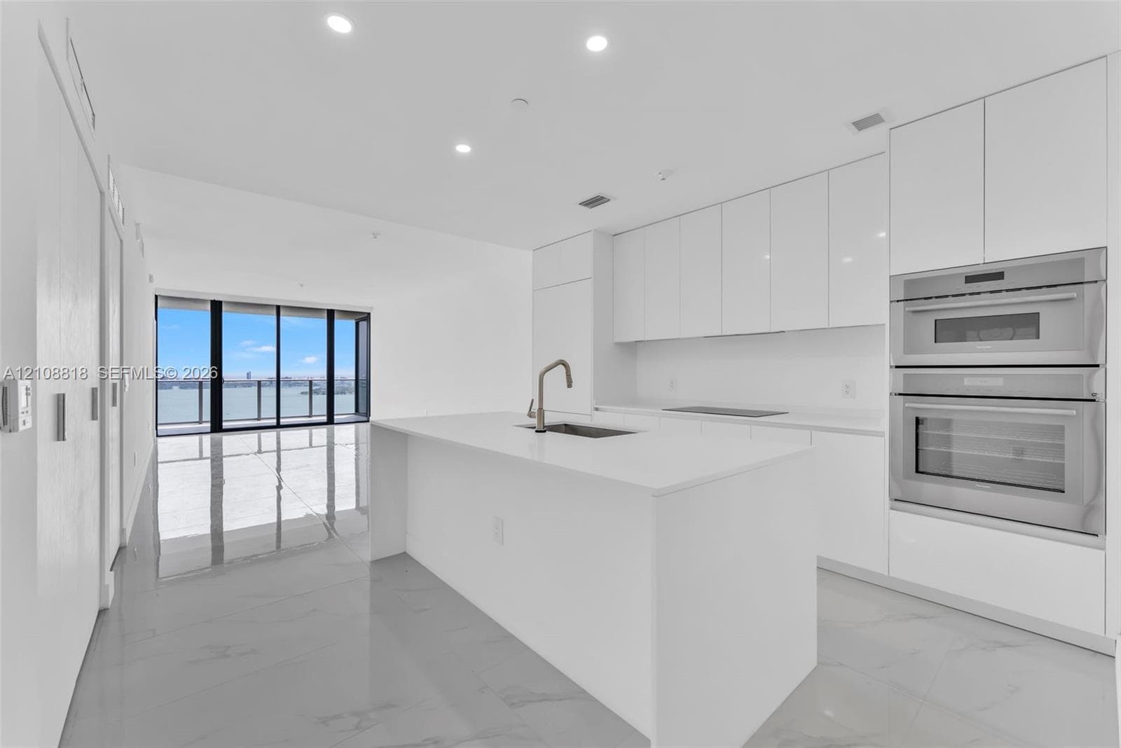 Modern kitchen featuring white flat-panel cabinetry, a central island with a solid-surface countertop, a stainless steel double wall oven, and large-format tile flooring