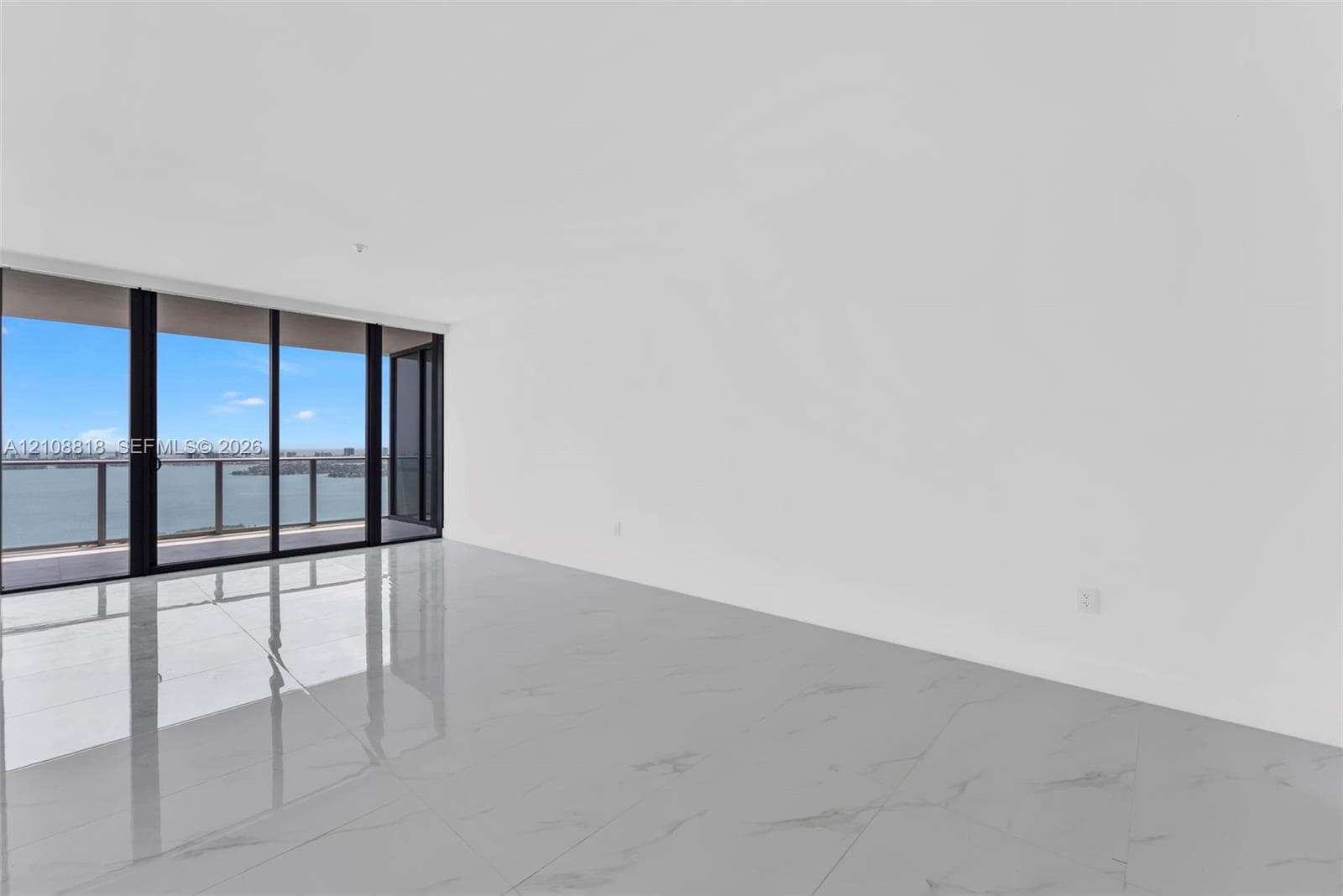 Open-concept interior featuring large-format polished tile flooring and floor-to-ceiling glass sliding doors opening to a private balcony with water scenery