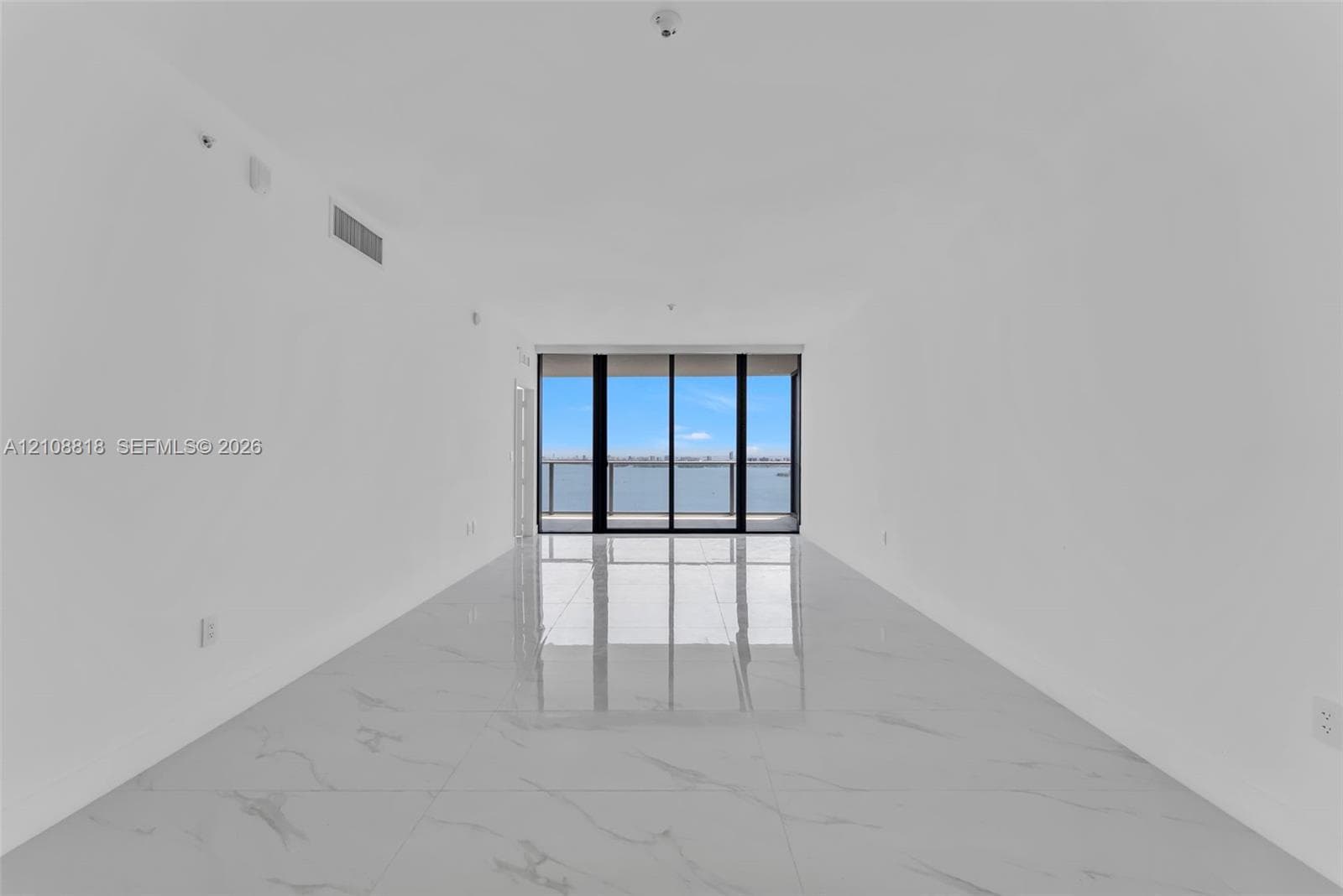 Expansive interior featuring large-format tile flooring and floor-to-ceiling glass sliding doors opening to a balcony