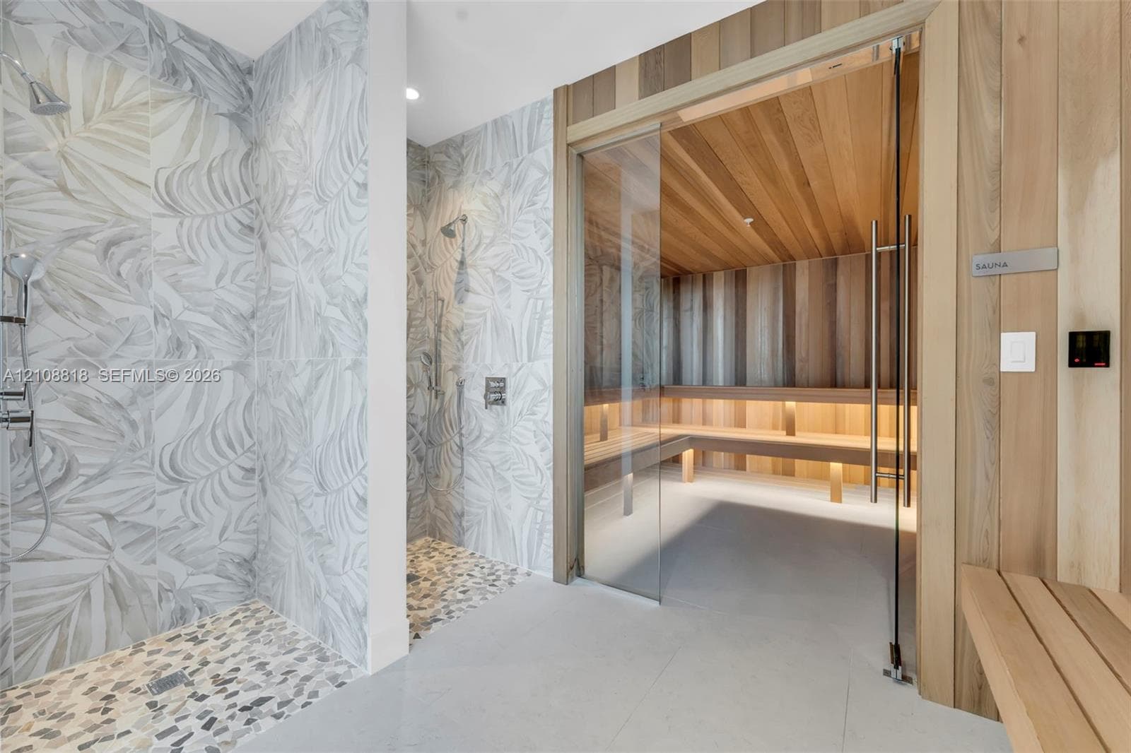 Custom sauna with integrated wood paneling and bench seating, paired with a walk-in shower featuring patterned tile walls, pebble flooring, and dual chrome showerheads