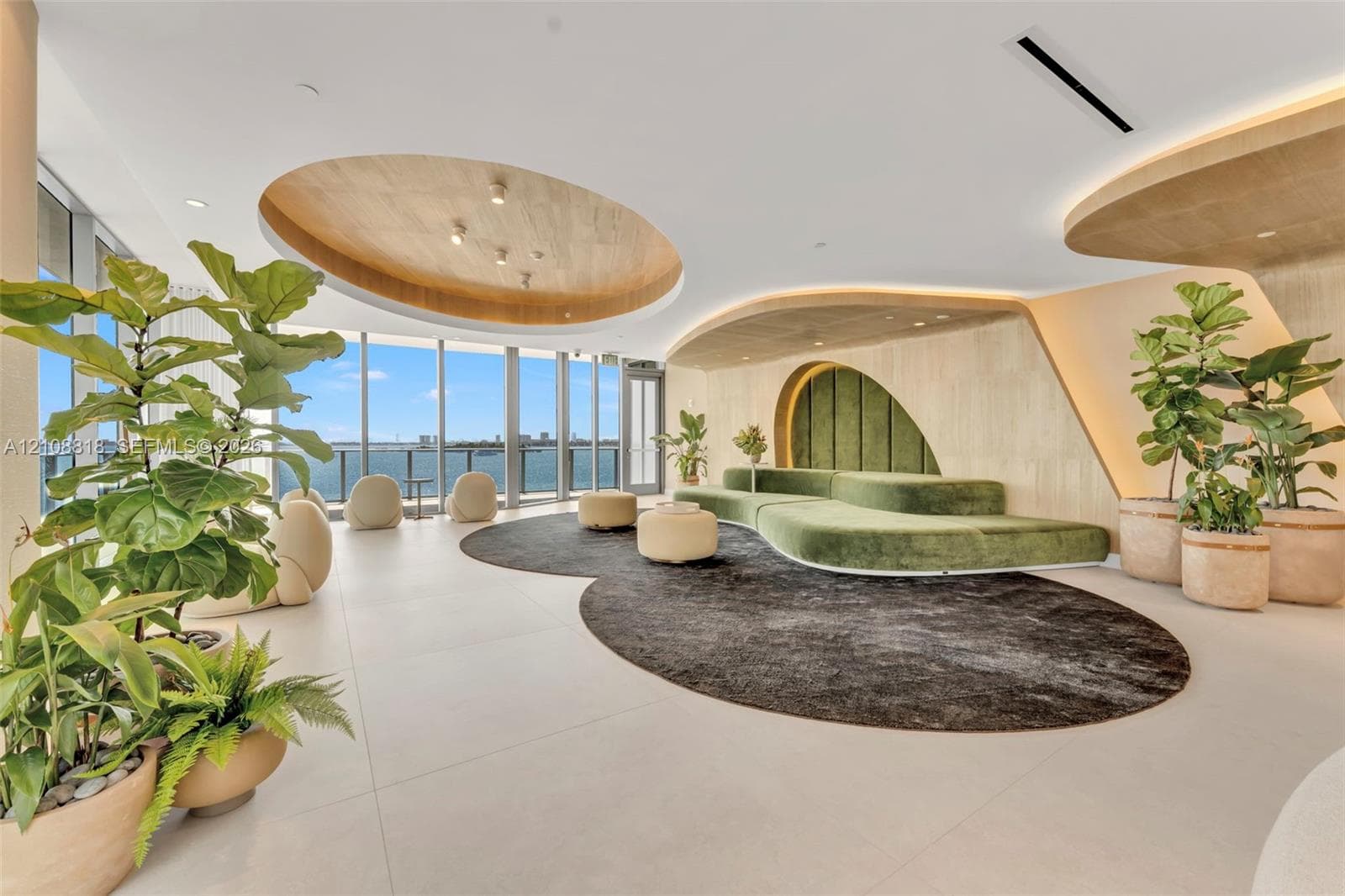 Floor-to-ceiling windows, circular recessed wood-finish ceiling detailing, expansive tile flooring, custom curved wood-paneled wall accent, and integrated cove lighting